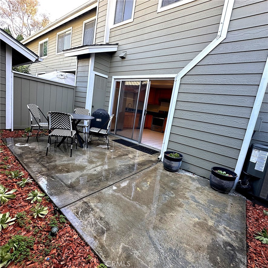 Concrete patio with striped outdoor seating beside a gray-sided home and open sliding glass door.
