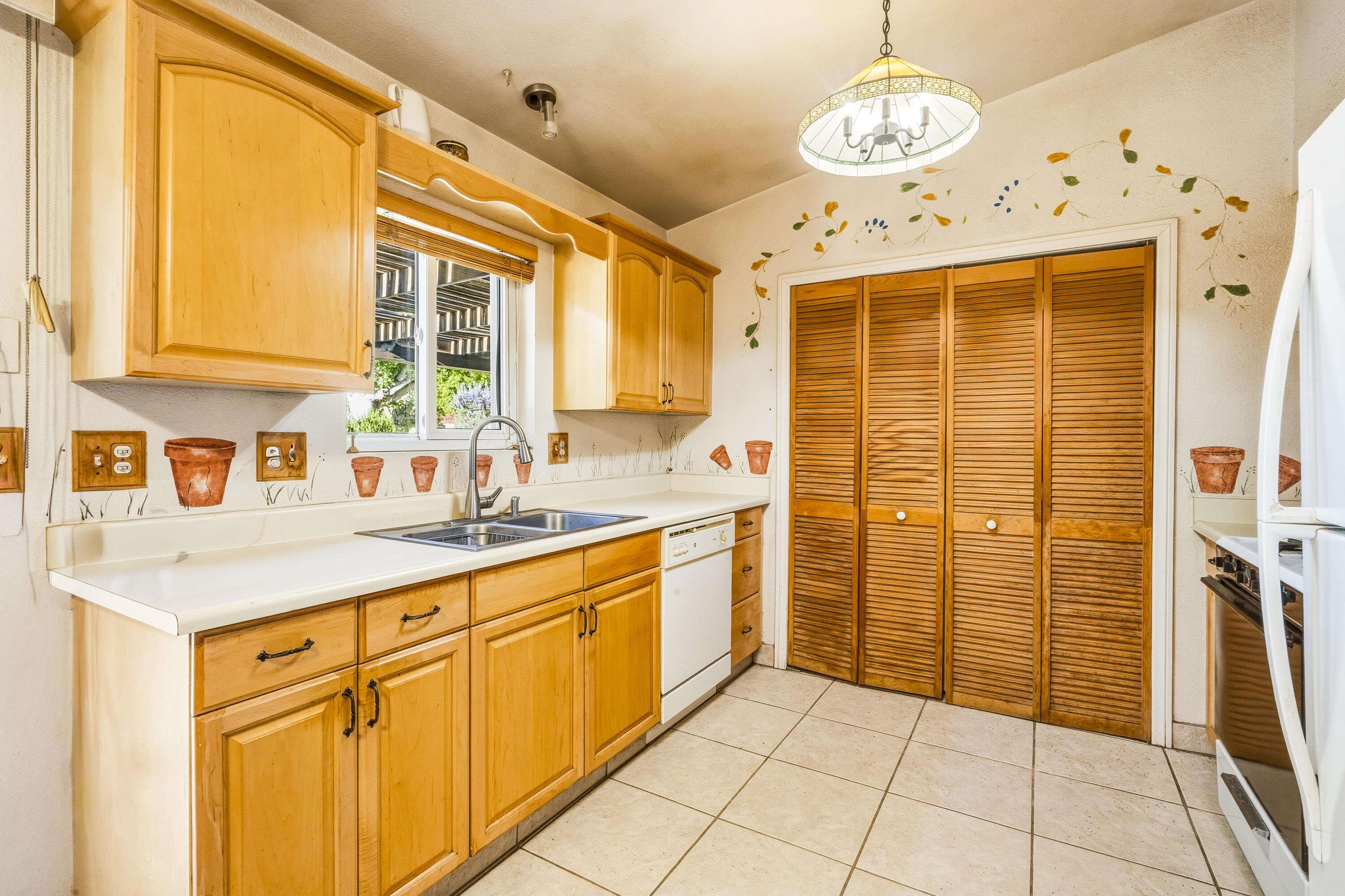 Kitchen with honey-colored cabinets, a double-basin sink beneath the window, and louvered pantry doors.