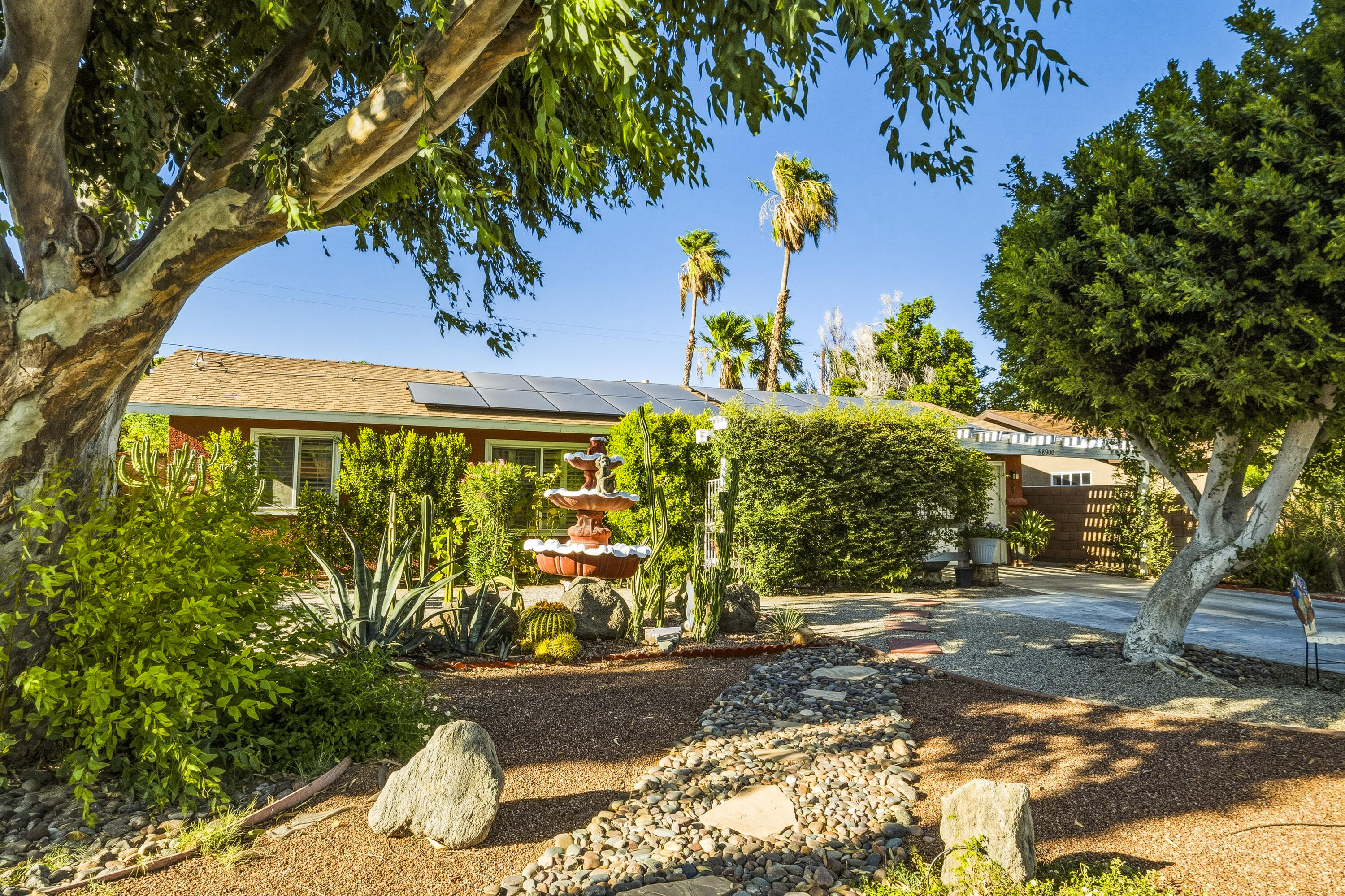 Single-story home with rooftop solar panels, desert landscaping, and a tiered fountain in the front yard.