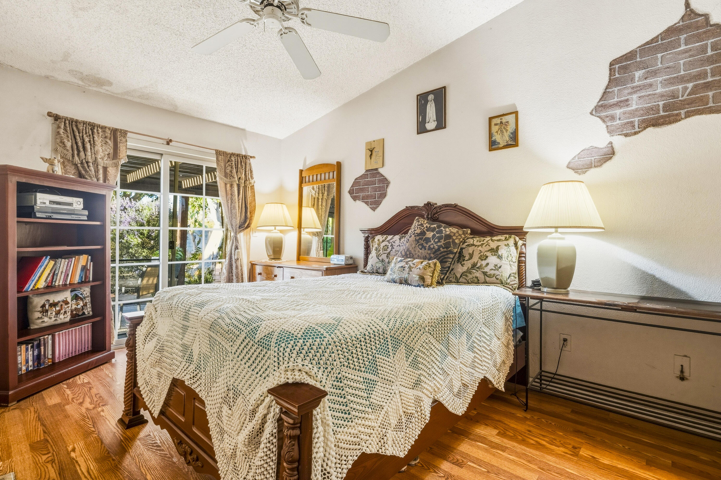 Bedroom with a large wooden bed, hardwood floors, sliding glass doors, and exposed-brick wall patches.
