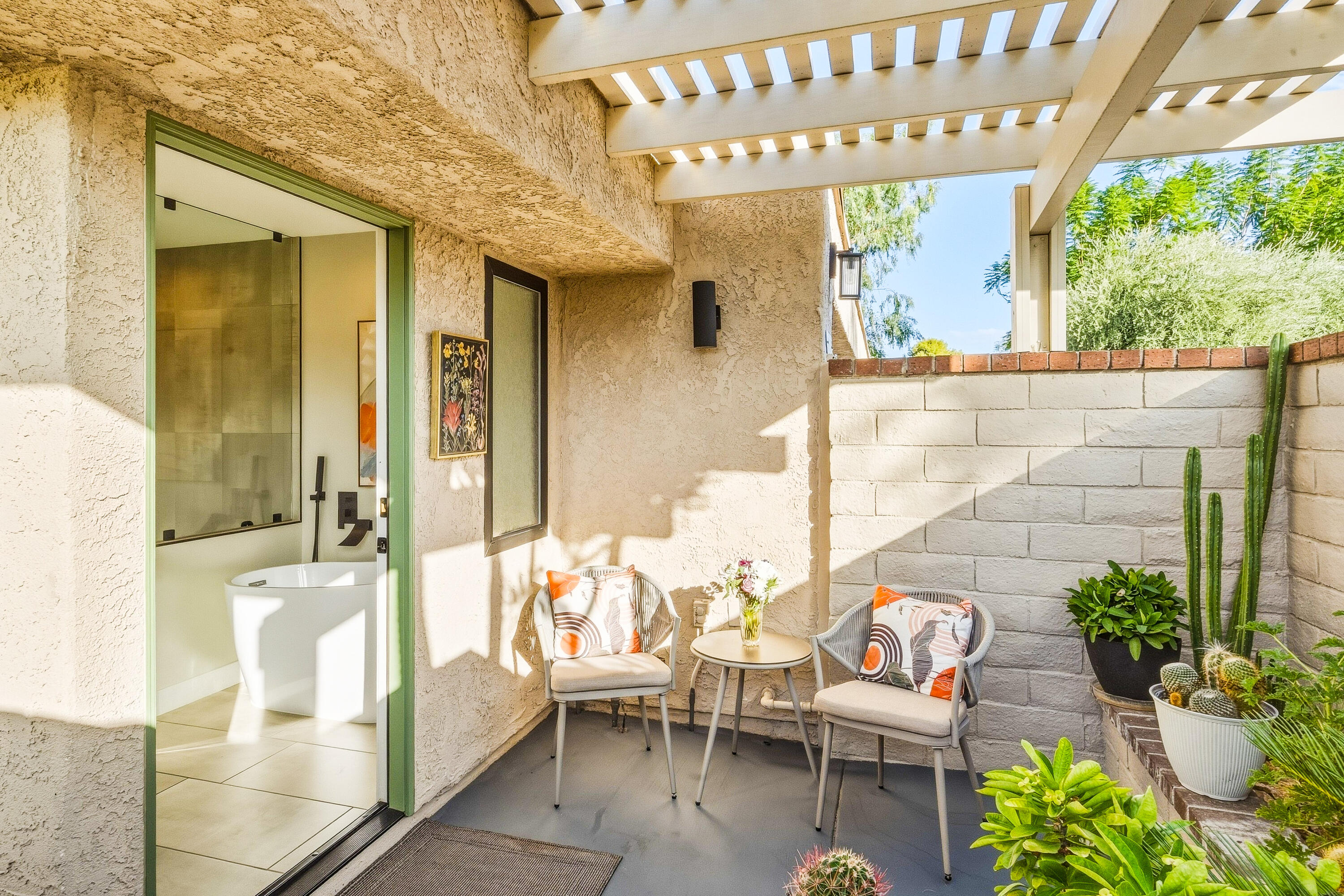 Private patio with pergola seating and a view into a bathroom with a freestanding tub.