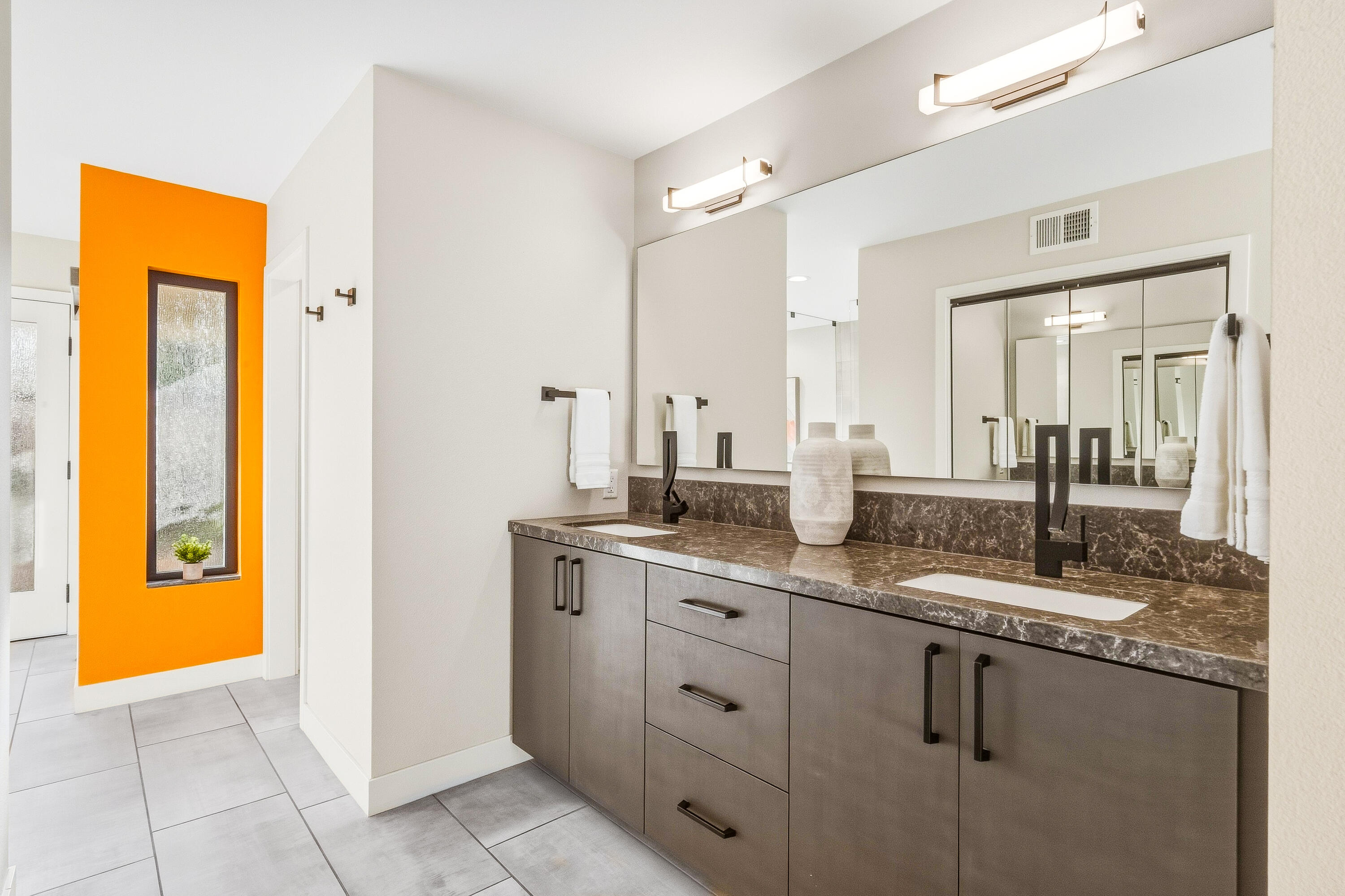 Modern double-sink bathroom vanity with a dark countertop and vivid orange accent wall.