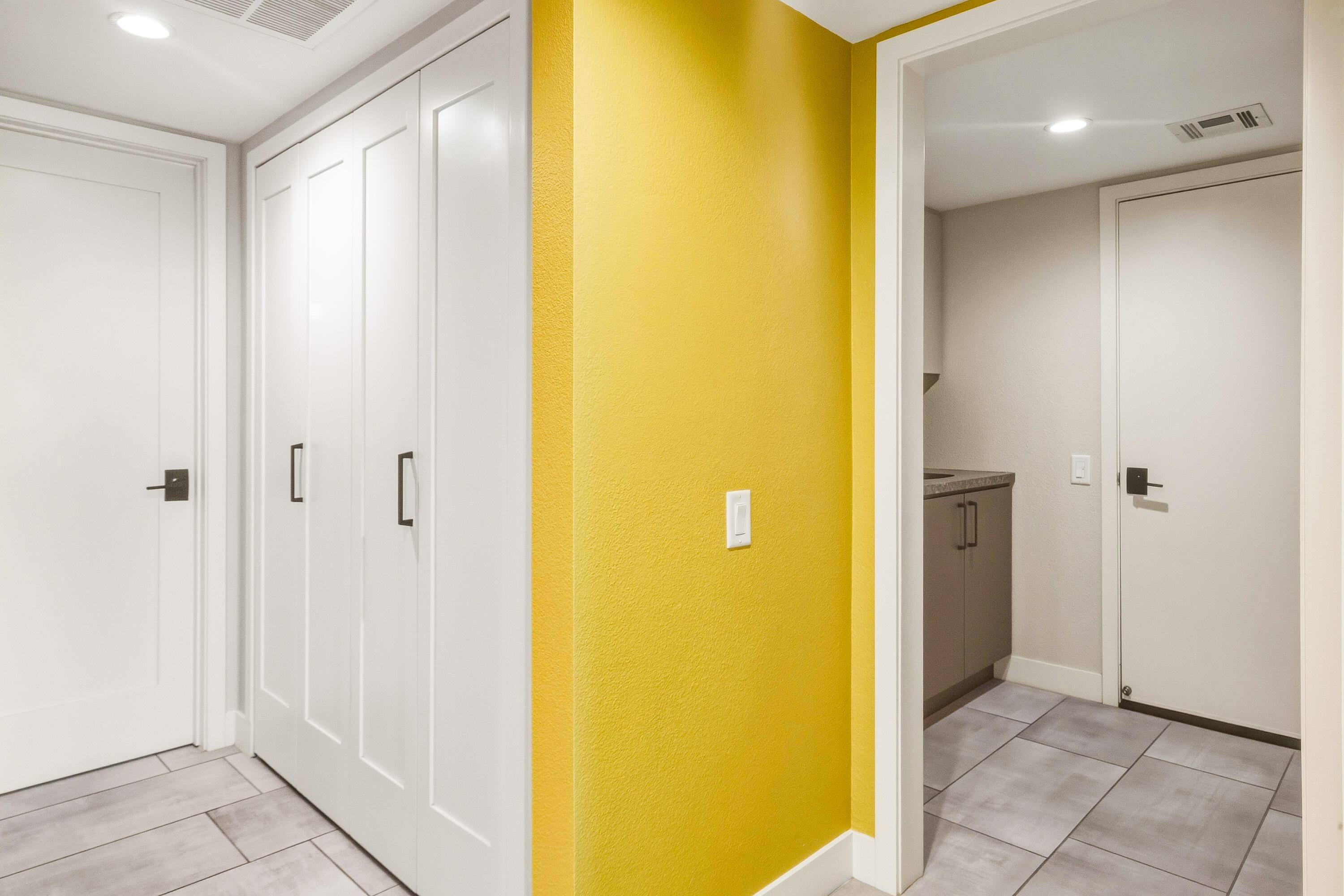 Hallway with white closet doors, gray tile flooring, and a bright yellow accent wall.