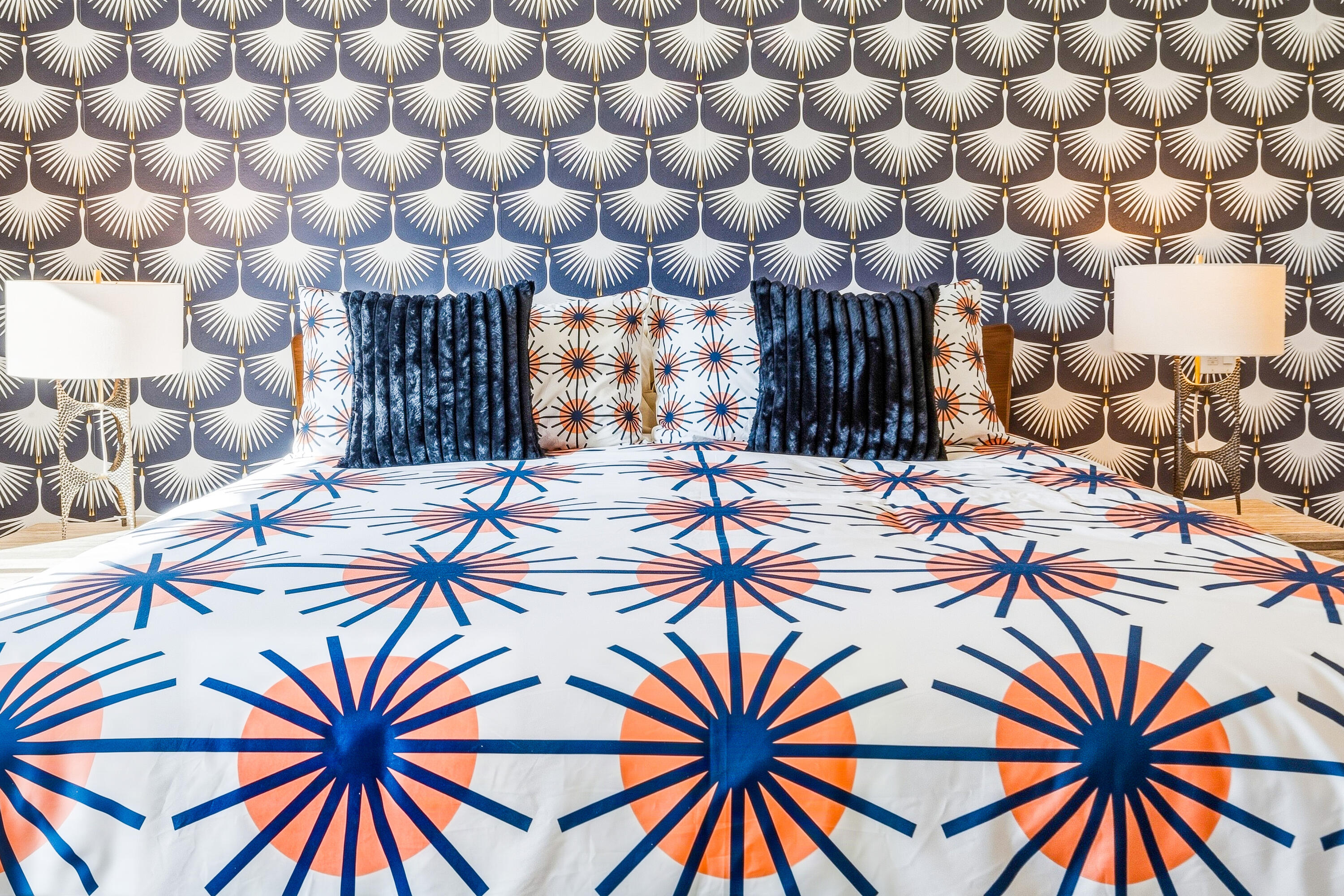 Bedroom with navy and coral starburst bedding, dark blue pillows, and bold patterned wallpaper.