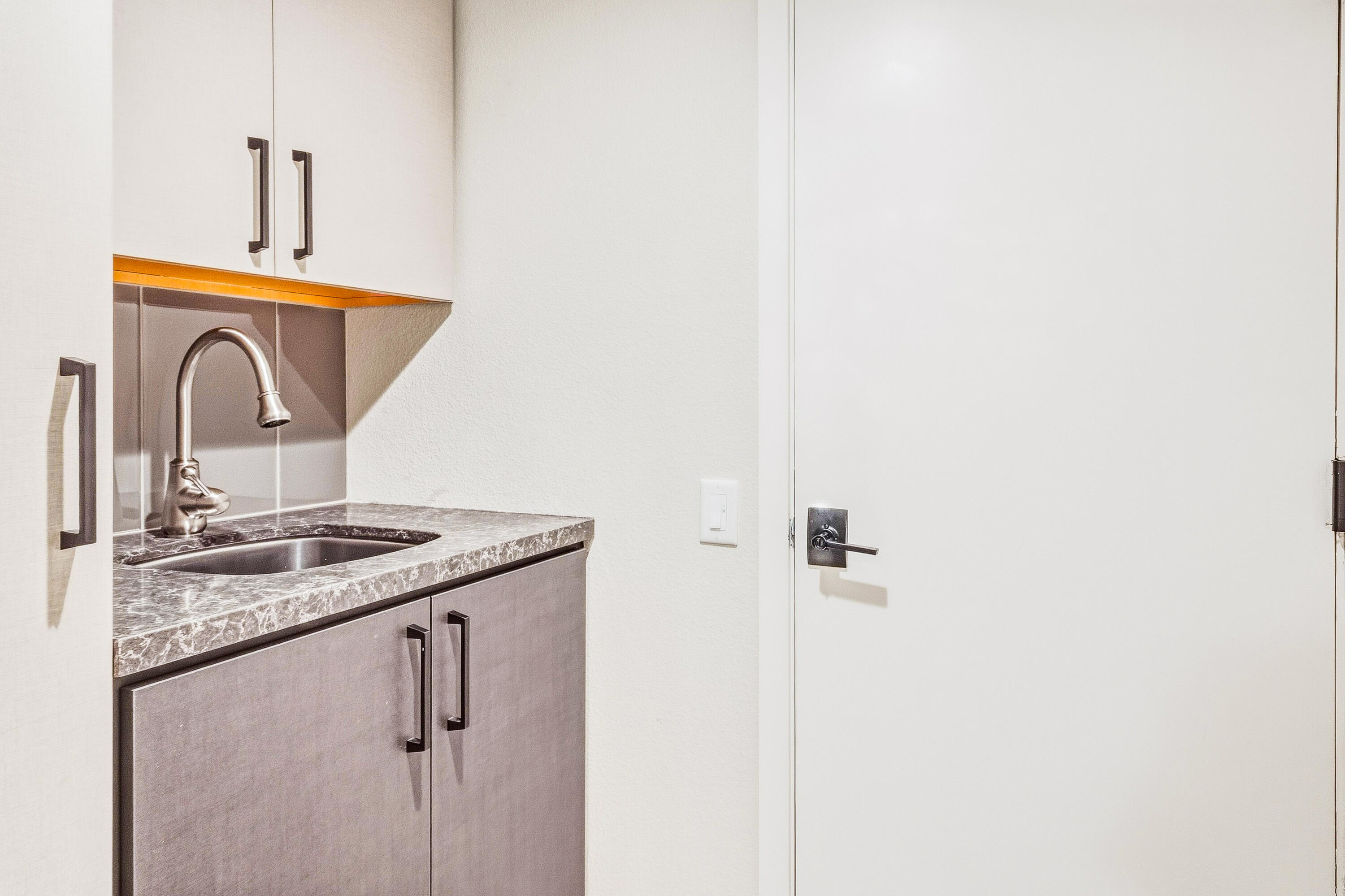 Built-in sink with gray cabinets, a veined stone countertop, and an arched metal faucet beside a white door.