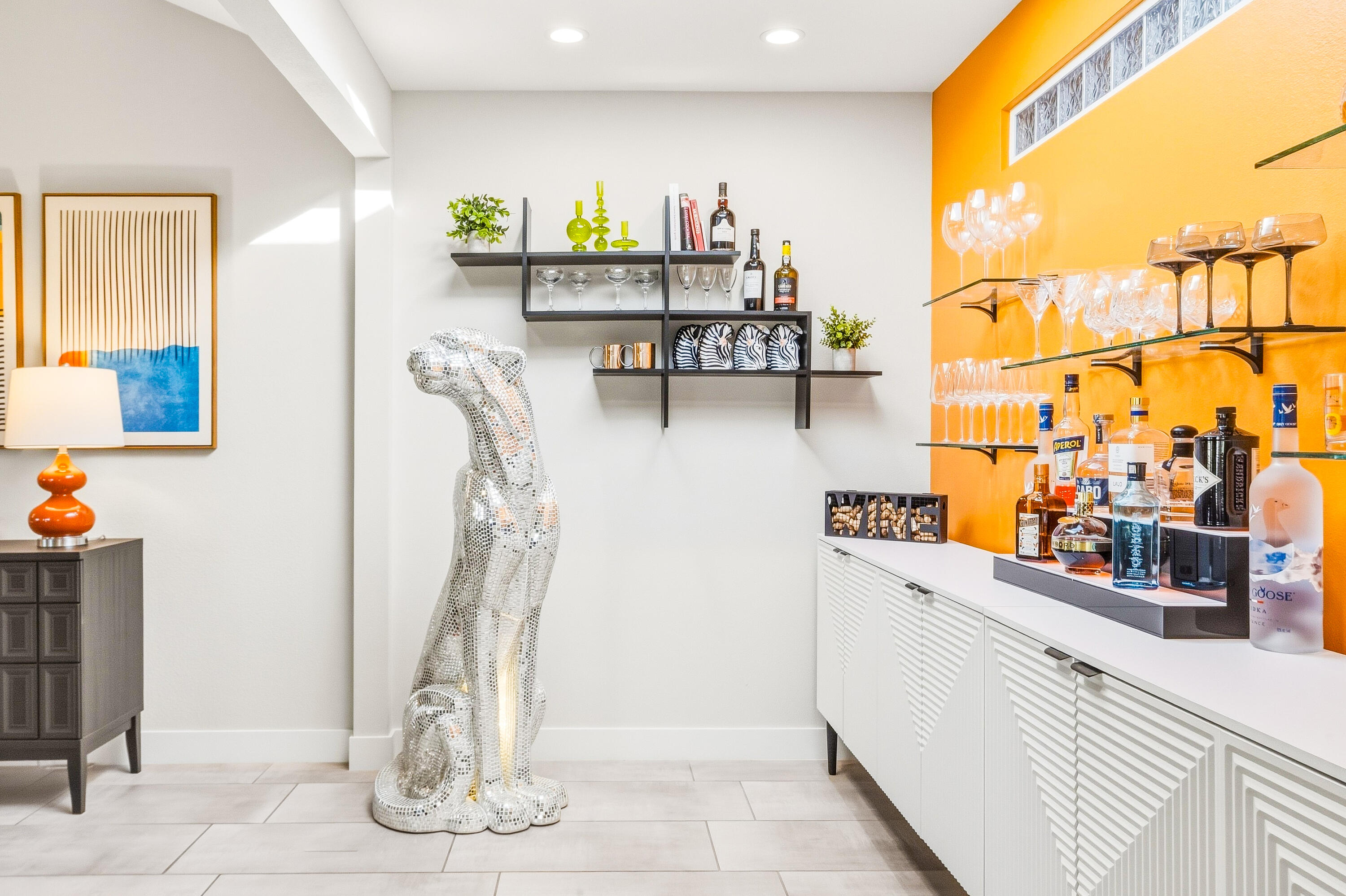 Interior bar with glass shelves, white cabinets, orange accent wall, and a mirrored dog sculpture.
