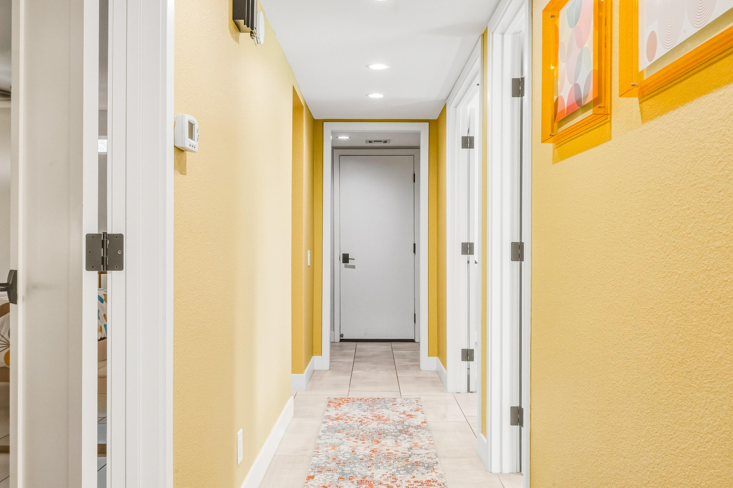 Yellow-walled hallway with white doorways, a patterned runner, and framed abstract art.