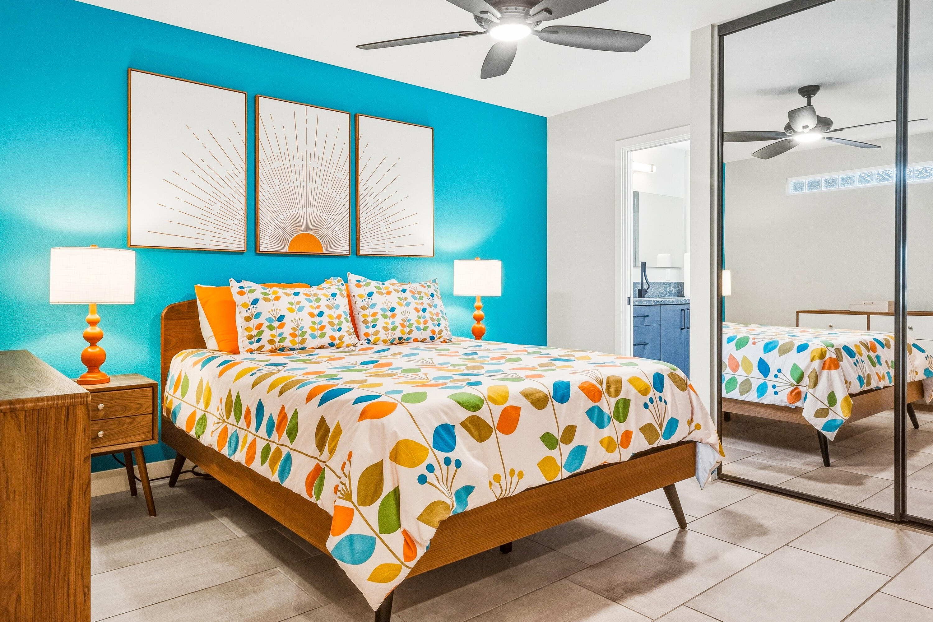 Staged bedroom with a colorful patterned bed, turquoise accent wall, and mirrored closet doors.