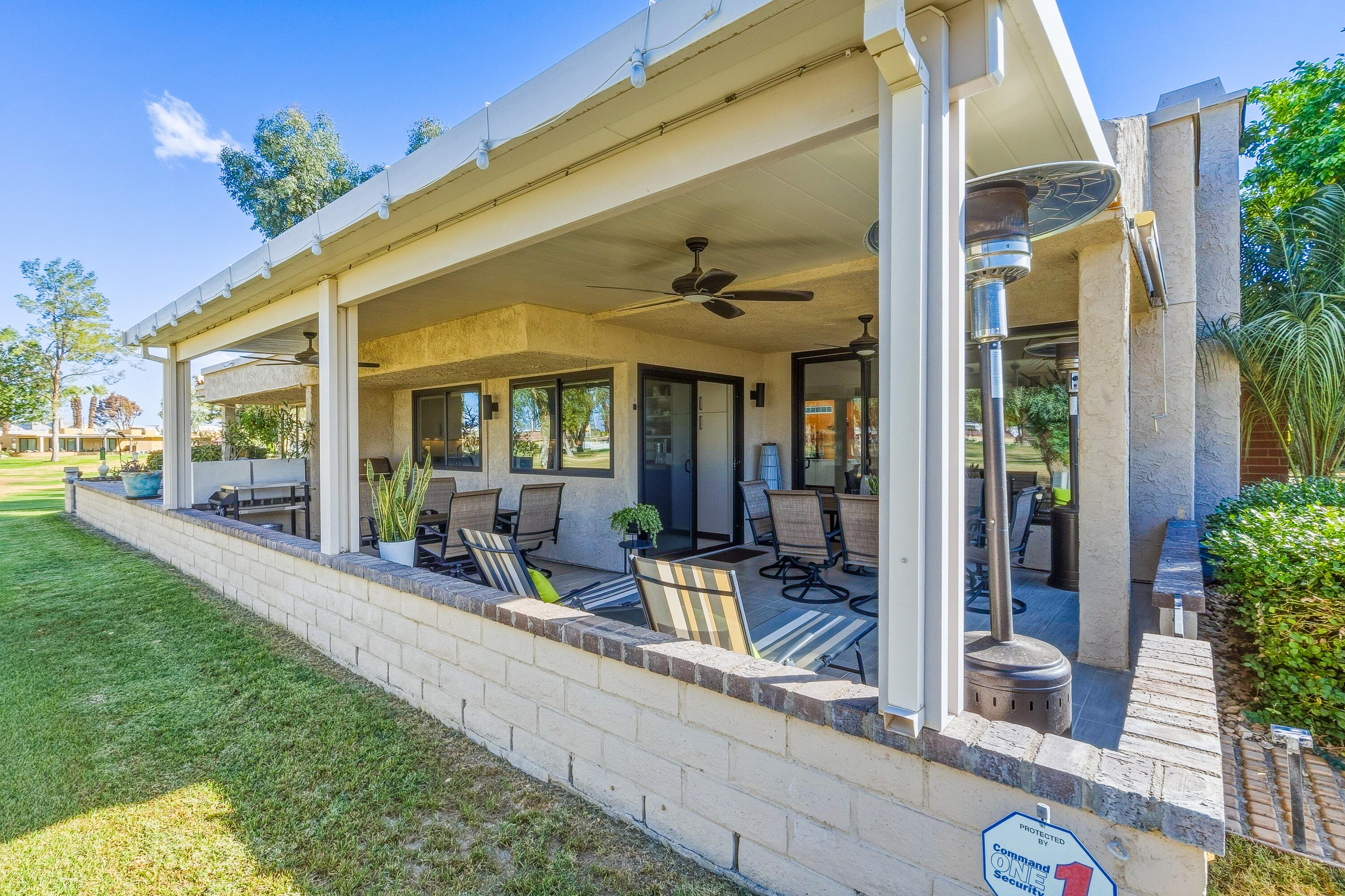 Covered patio with outdoor seating, ceiling fans, and a patio heater beside the lawn.