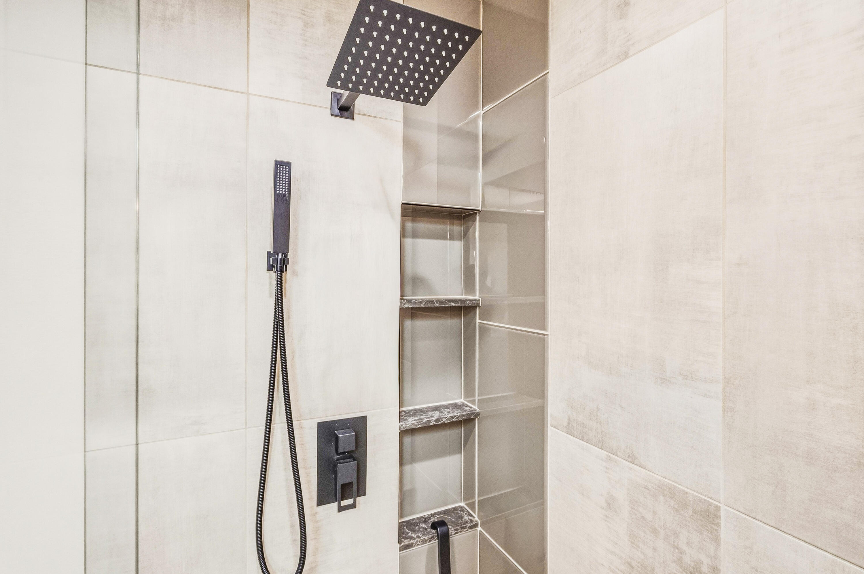 Walk-in shower with a black rainfall showerhead, handheld sprayer, and built-in tiled shelves.
