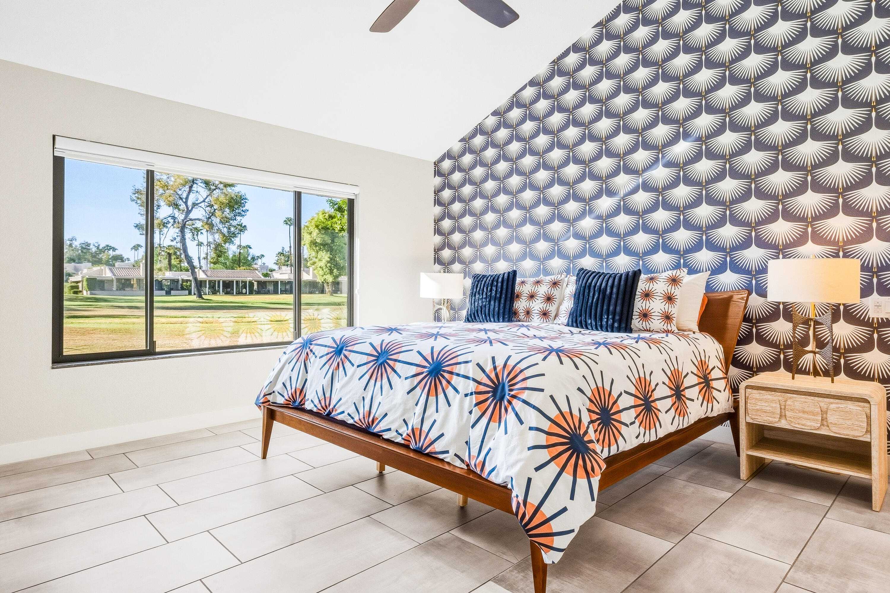 Furnished bedroom with bold patterned accent wall, starburst bedding, and a large window overlooking green grounds.