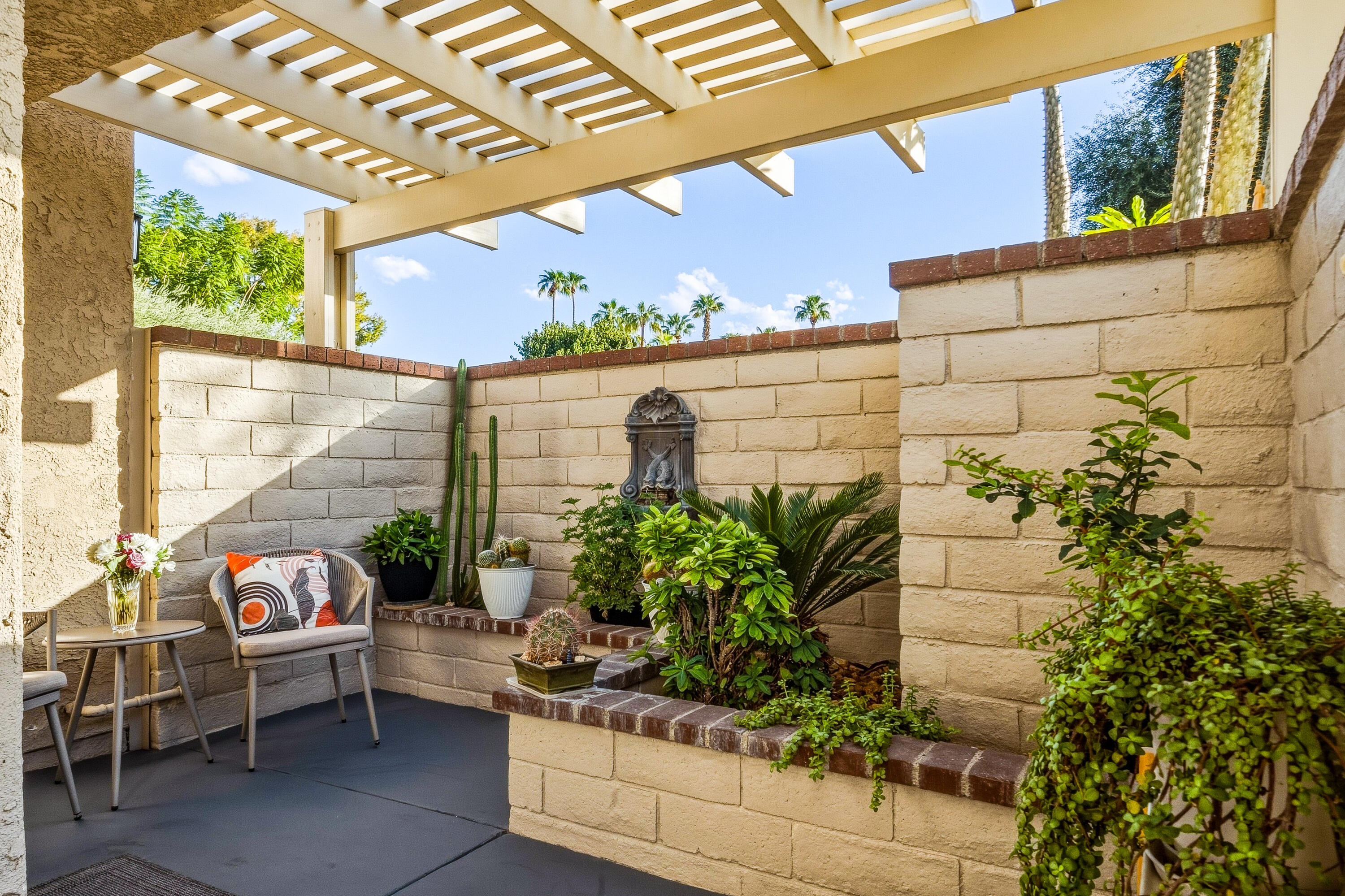Patio with pergola, cushioned chairs, raised planters, cacti, and a decorative wall fountain.