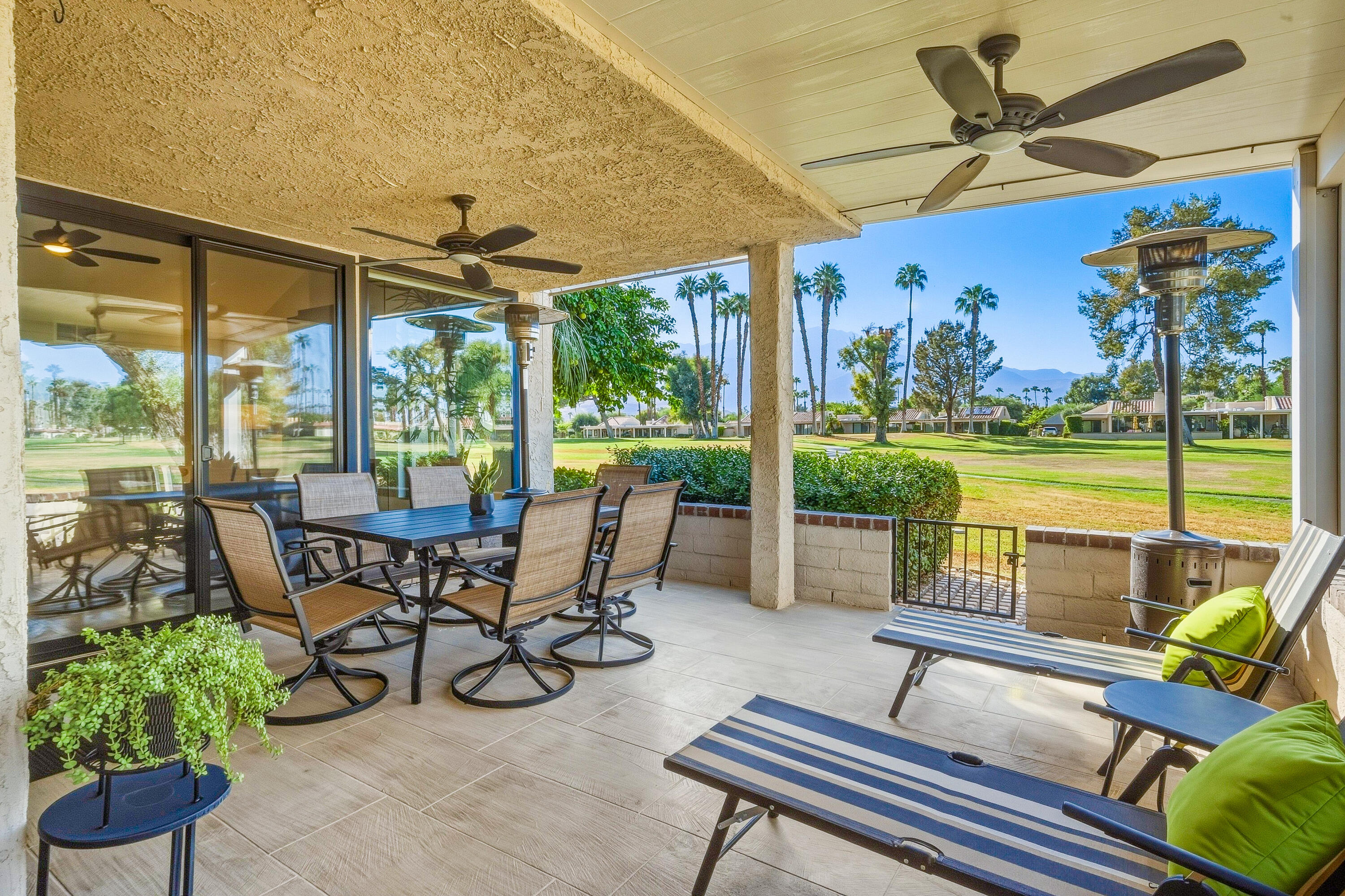 Covered patio with outdoor dining and lounge furniture overlooking a golf course and distant mountains.