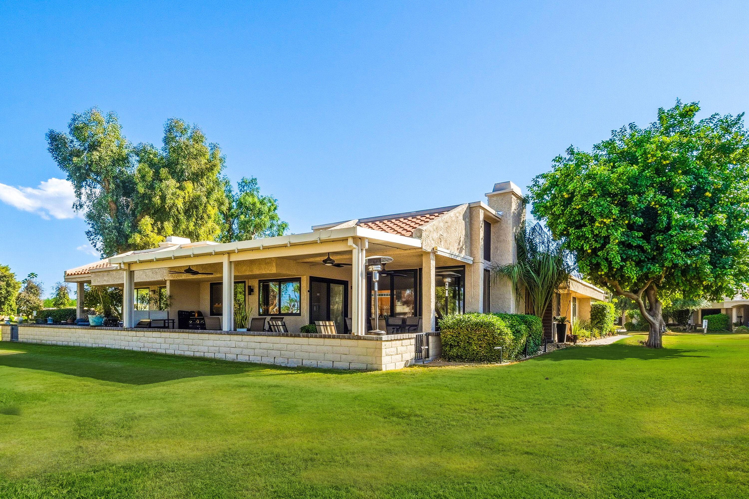 Home’s rear exterior with a covered patio, outdoor seating, and a wide green lawn.