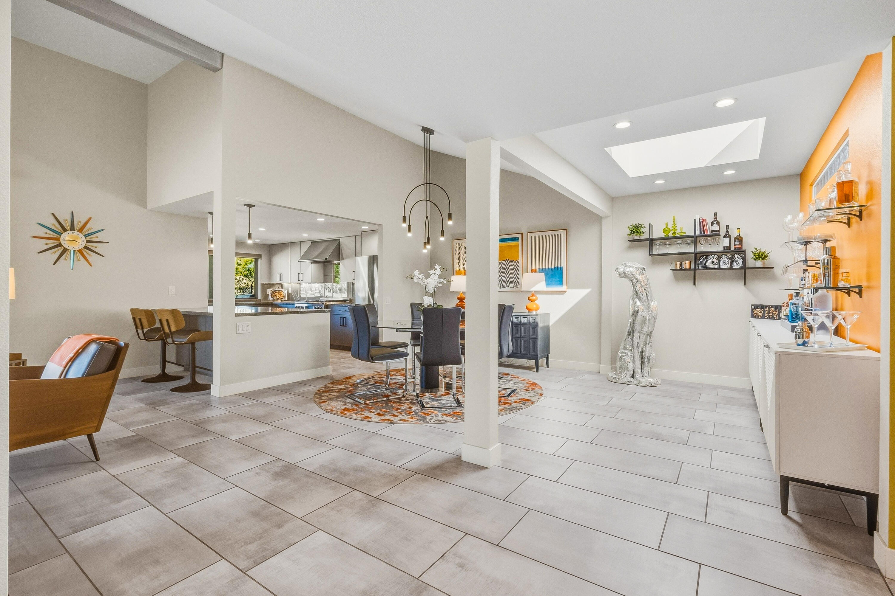 Open-plan dining area with a skylight, round patterned rug, and orange bar wall.