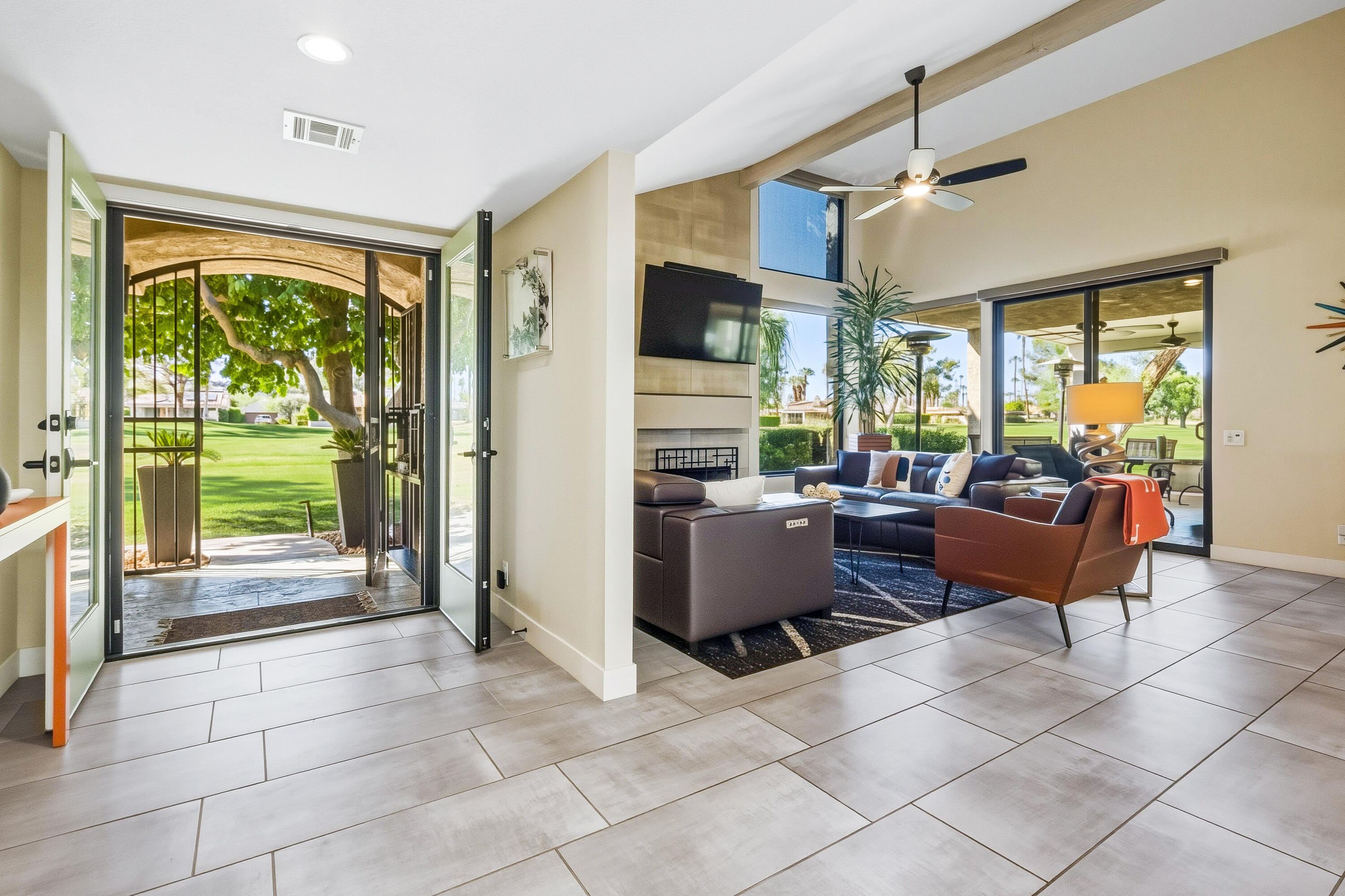 Living room with a fireplace and wide-open doors overlooking a leafy lawn.
