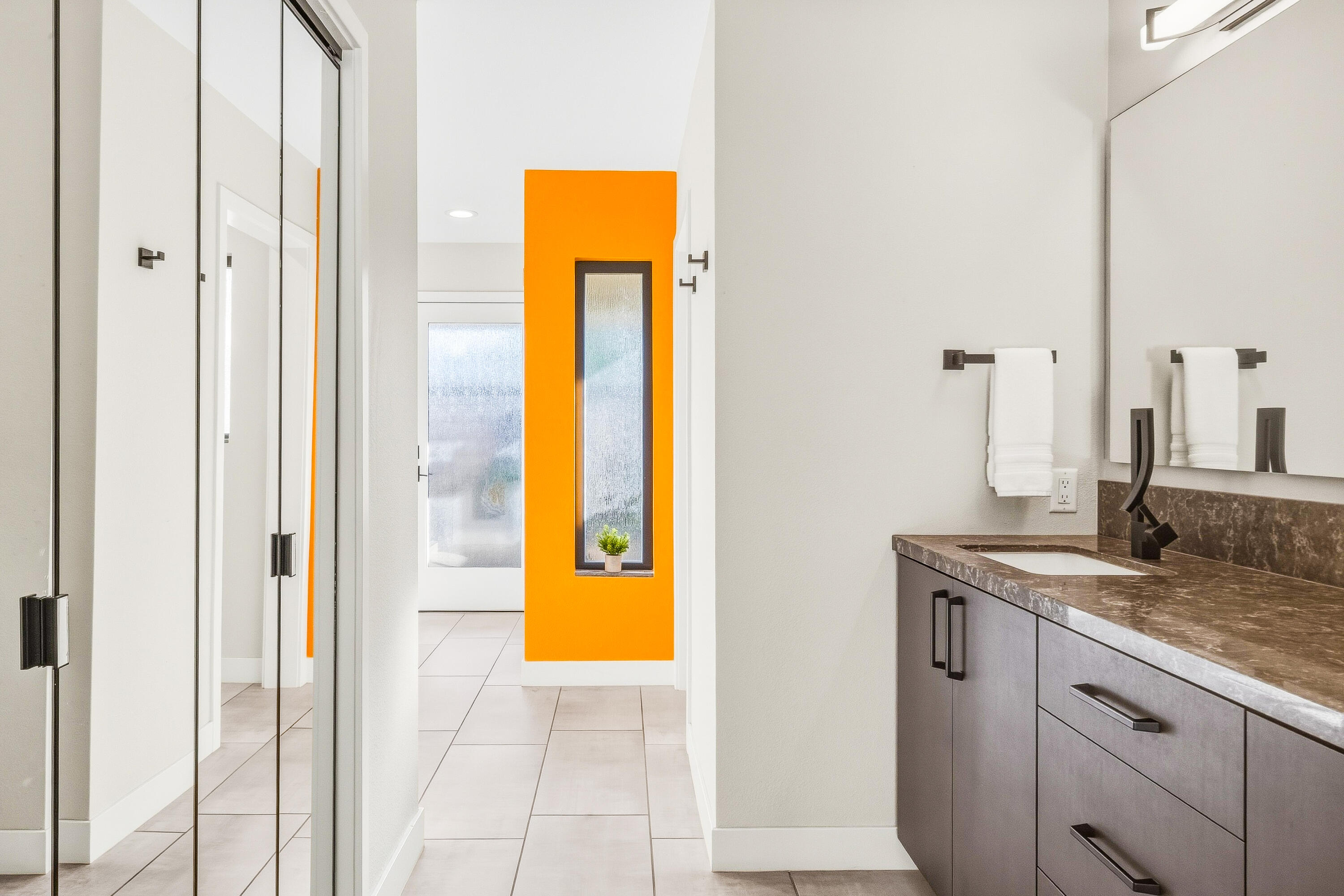 Modern bathroom with a dark wood vanity and vivid orange accent wall with a narrow window.