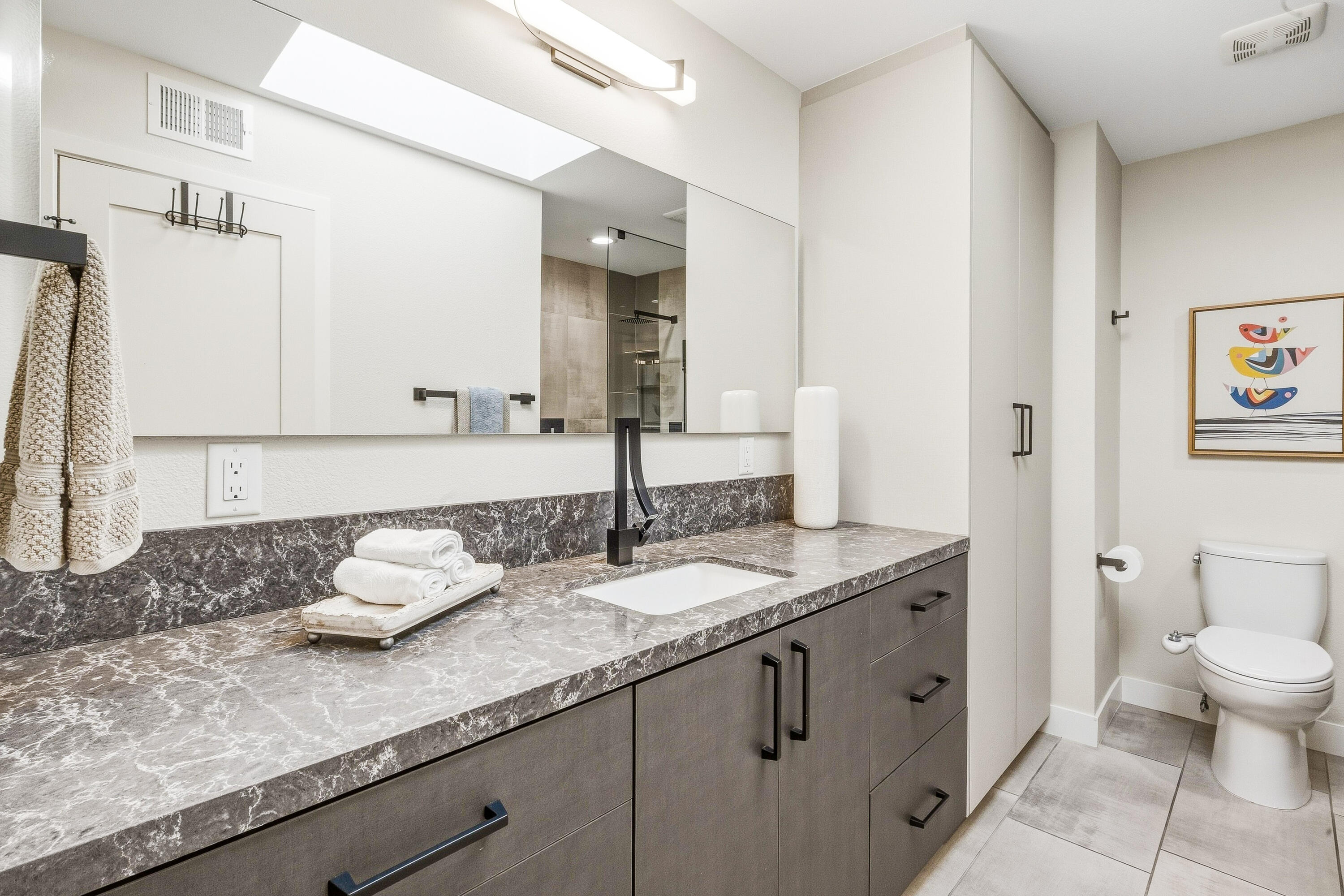 Modern bathroom with a marble vanity, black faucet, mirrored shower, and colorful framed artwork.