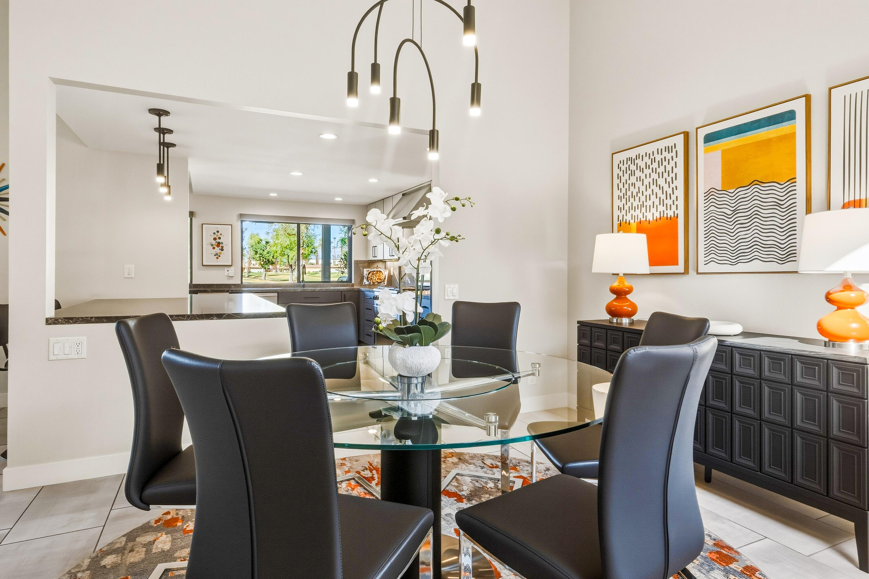 Staged dining room with a glass table, dark chairs, and an open view into the kitchen.