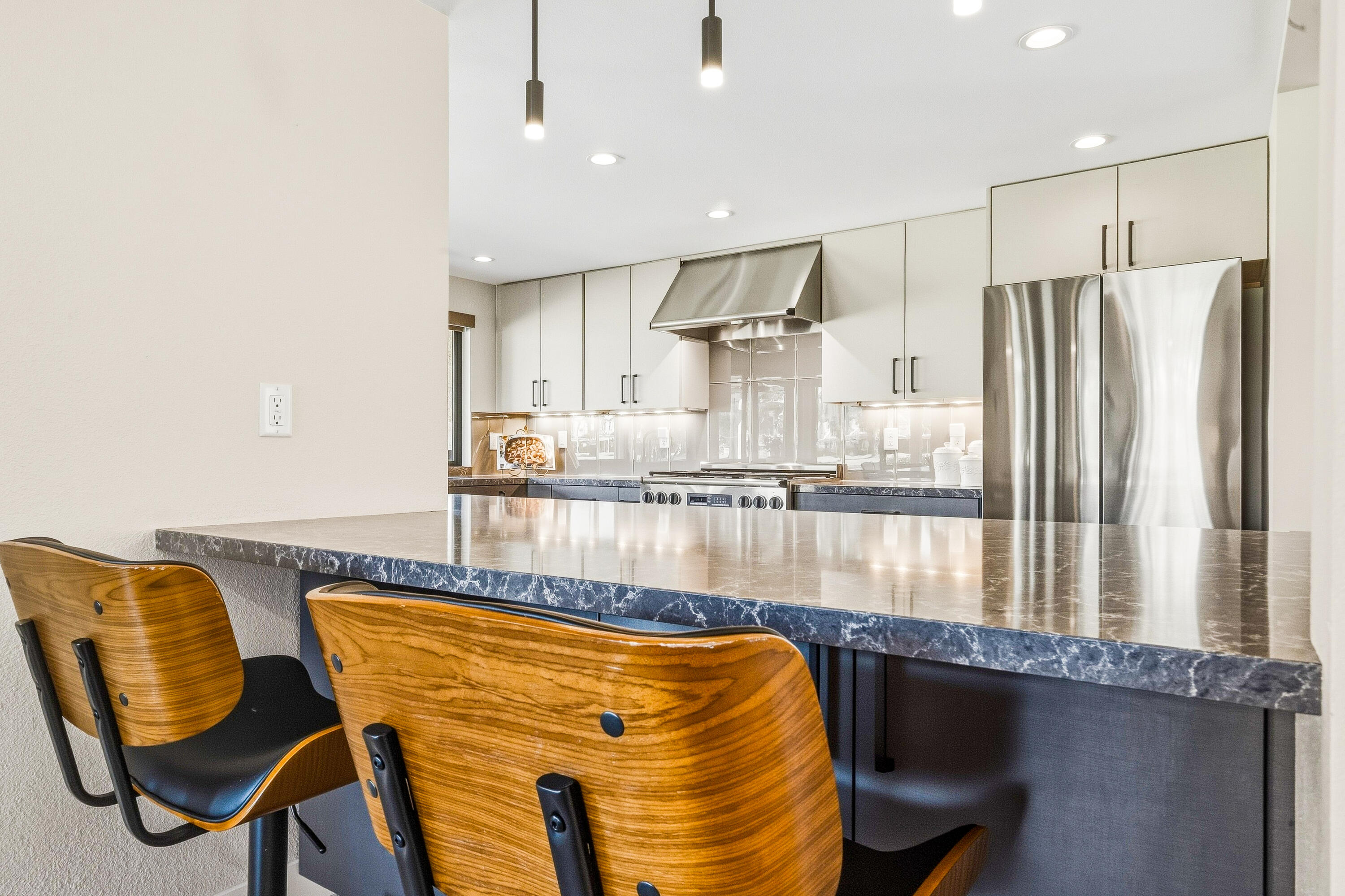 Modern kitchen with a large stone island, stainless steel appliances, and two wood bar stools.