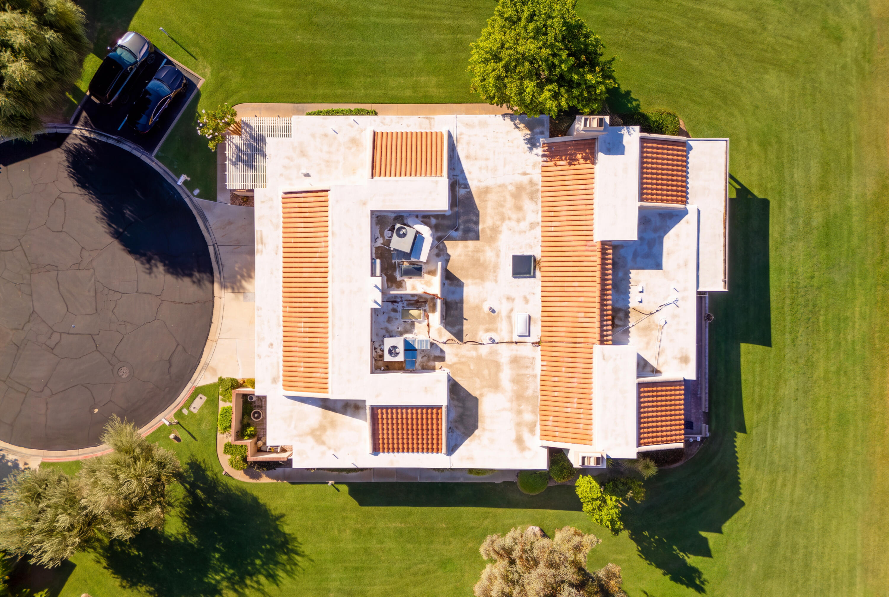 Aerial view of a home's flat roof, terracotta tile sections, surrounding lawn, and circular driveway.
