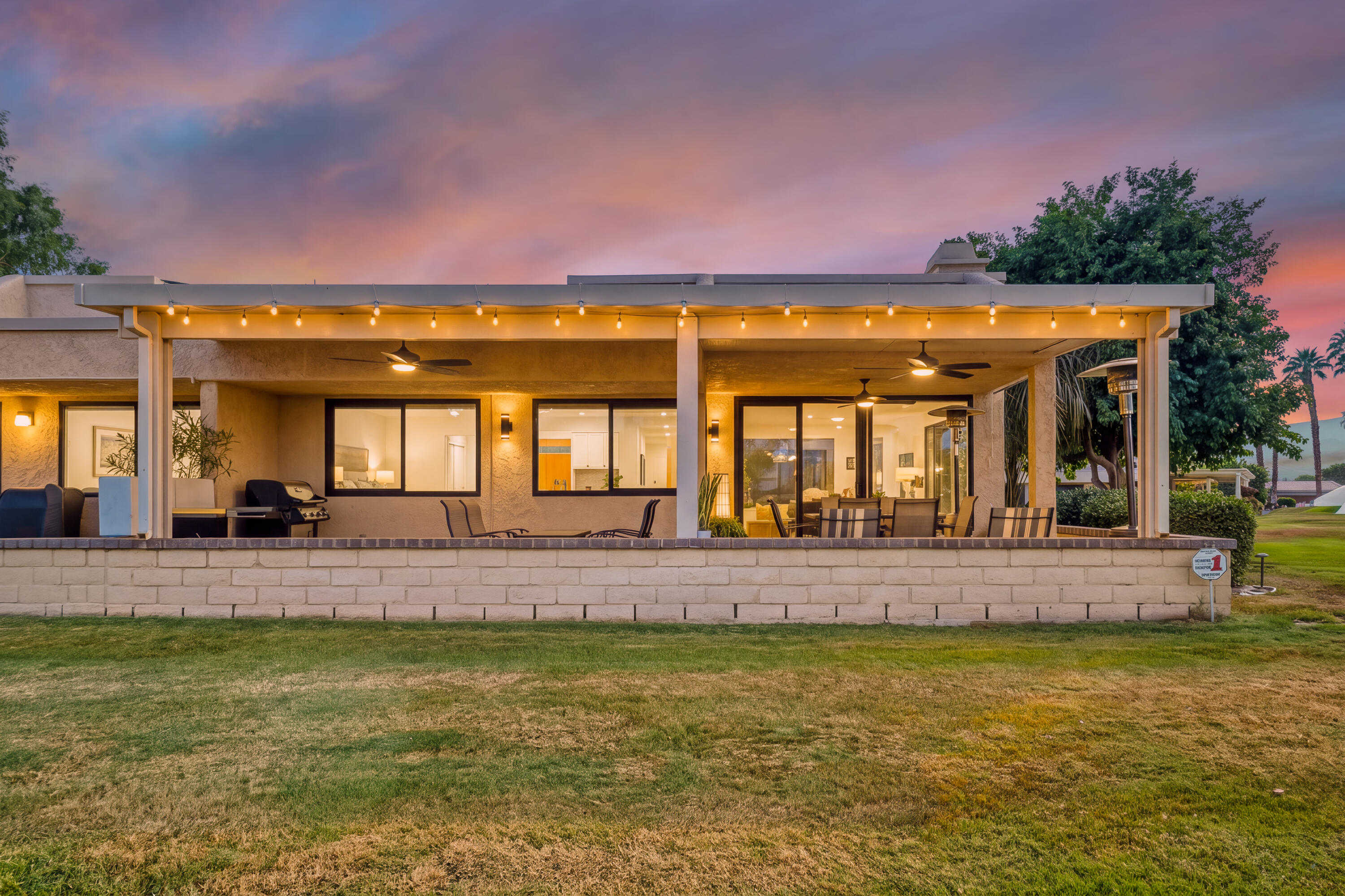 Home’s covered rear patio with string lights, ceiling fans, and outdoor dining furniture at dusk.