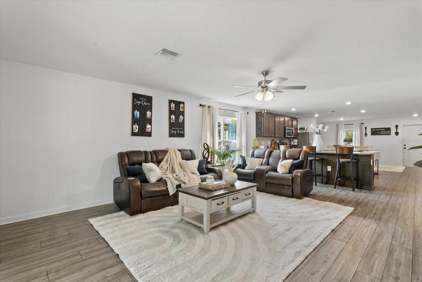 Living room with leather sofas, a patterned rug, and an open kitchen with a dark-cabinet island.