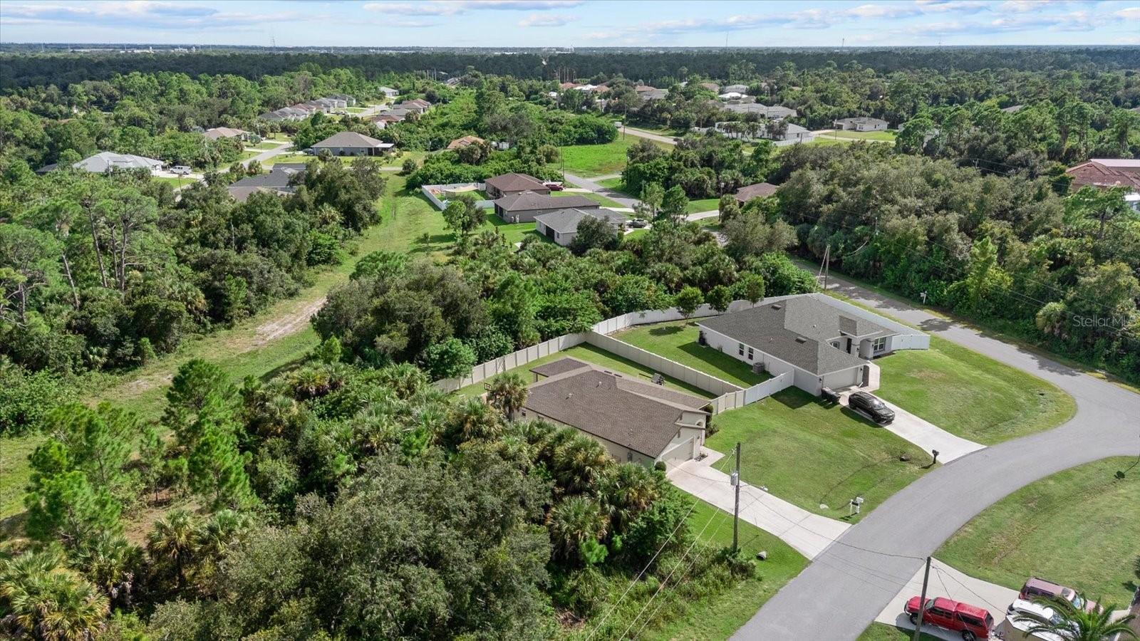 Aerial view of a single-story home with a fenced backyard beside a wooded lot.