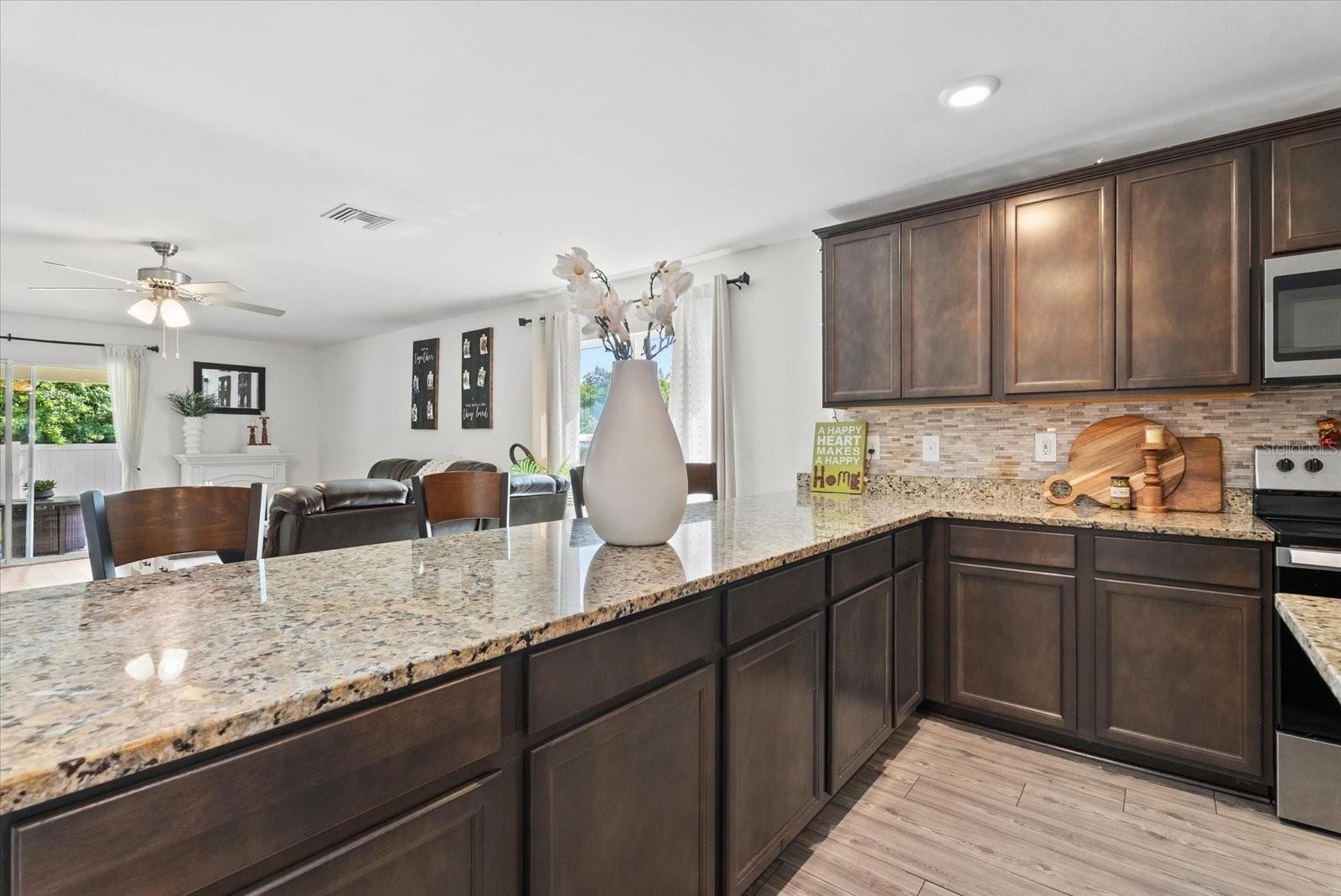 Kitchen with dark wood cabinets, granite counters, and a breakfast bar overlooking the living area.