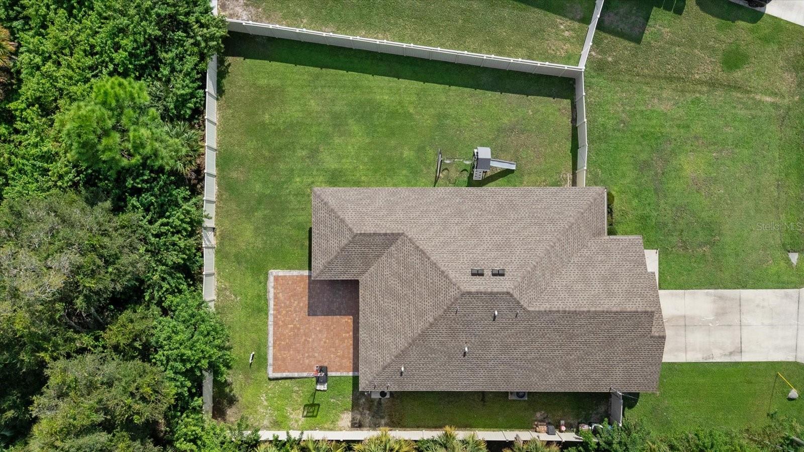 Aerial view of a home with a fenced grassy backyard, playset, and brick patio.