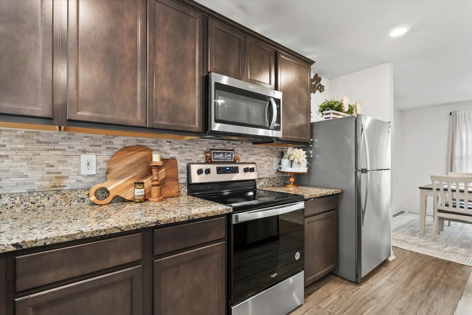 Kitchen with dark paneled cabinets, granite counters, and stainless steel appliances.