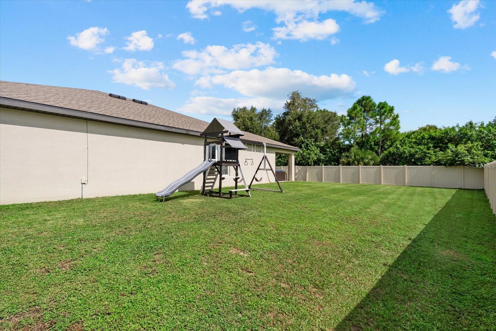 Fenced backyard with a large lawn and children's playset beside the home.