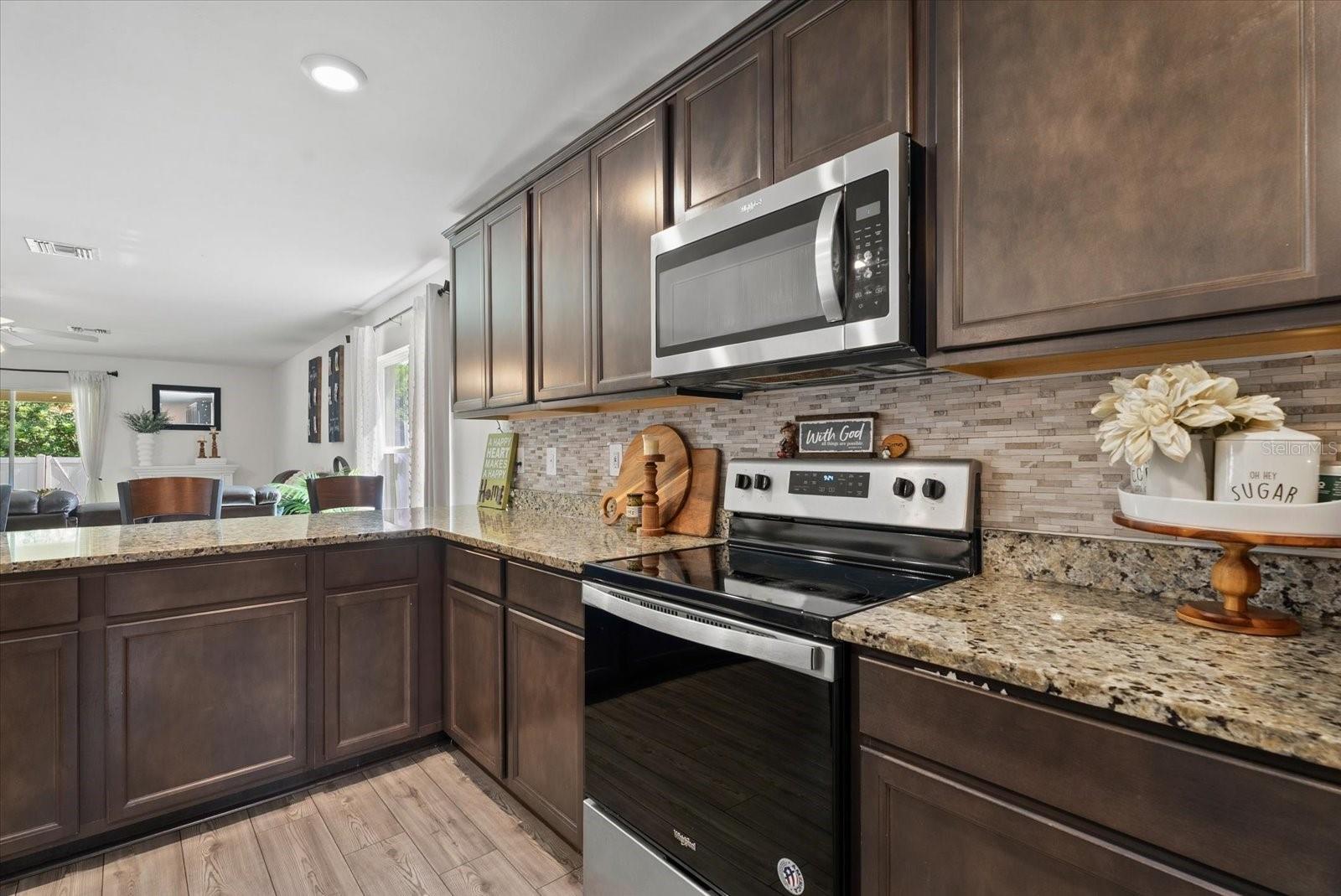 Kitchen with dark cabinetry, granite counters, mosaic backsplash, and stainless steel appliances.