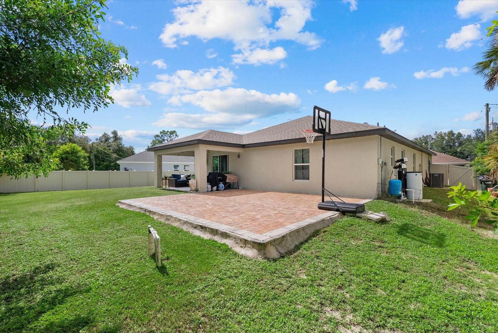 Home’s backyard with a brick-paver patio, basketball hoop, covered lanai, and fenced lawn.
