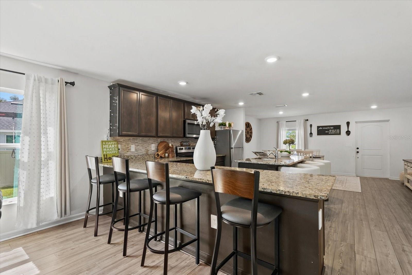 Open kitchen with dark cabinets, granite island, bar stools, and dining area.