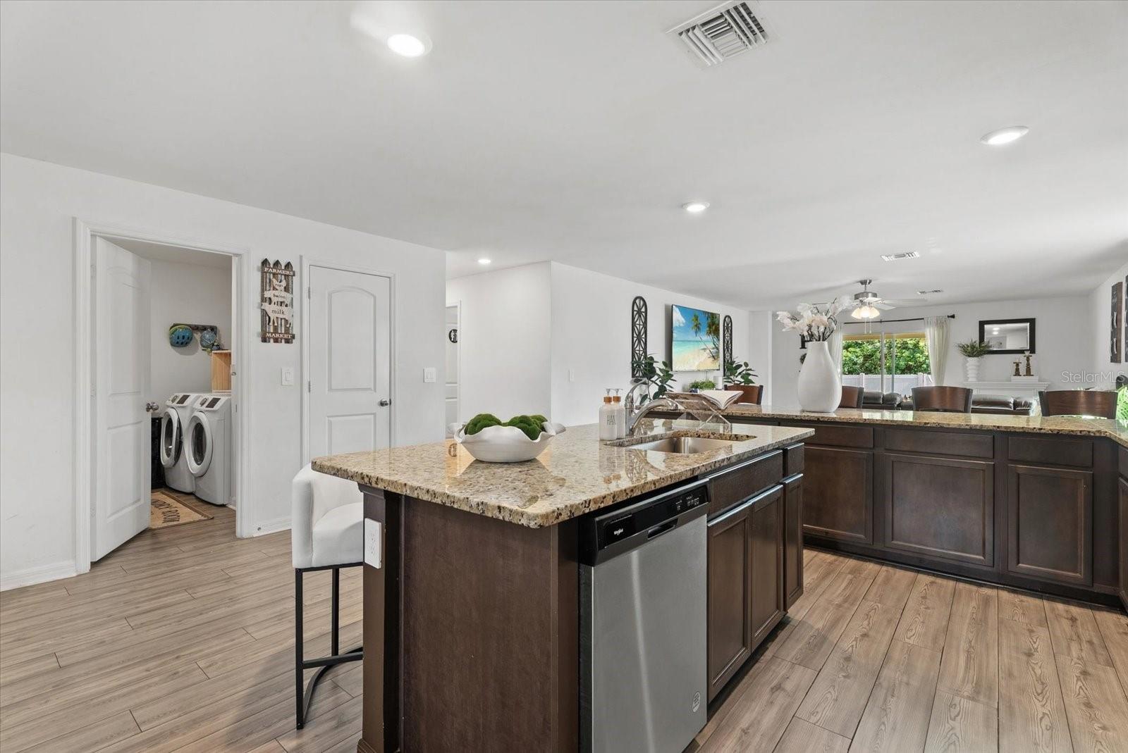 Open-plan kitchen with a granite island, dark wood cabinets, and a view into the living area.