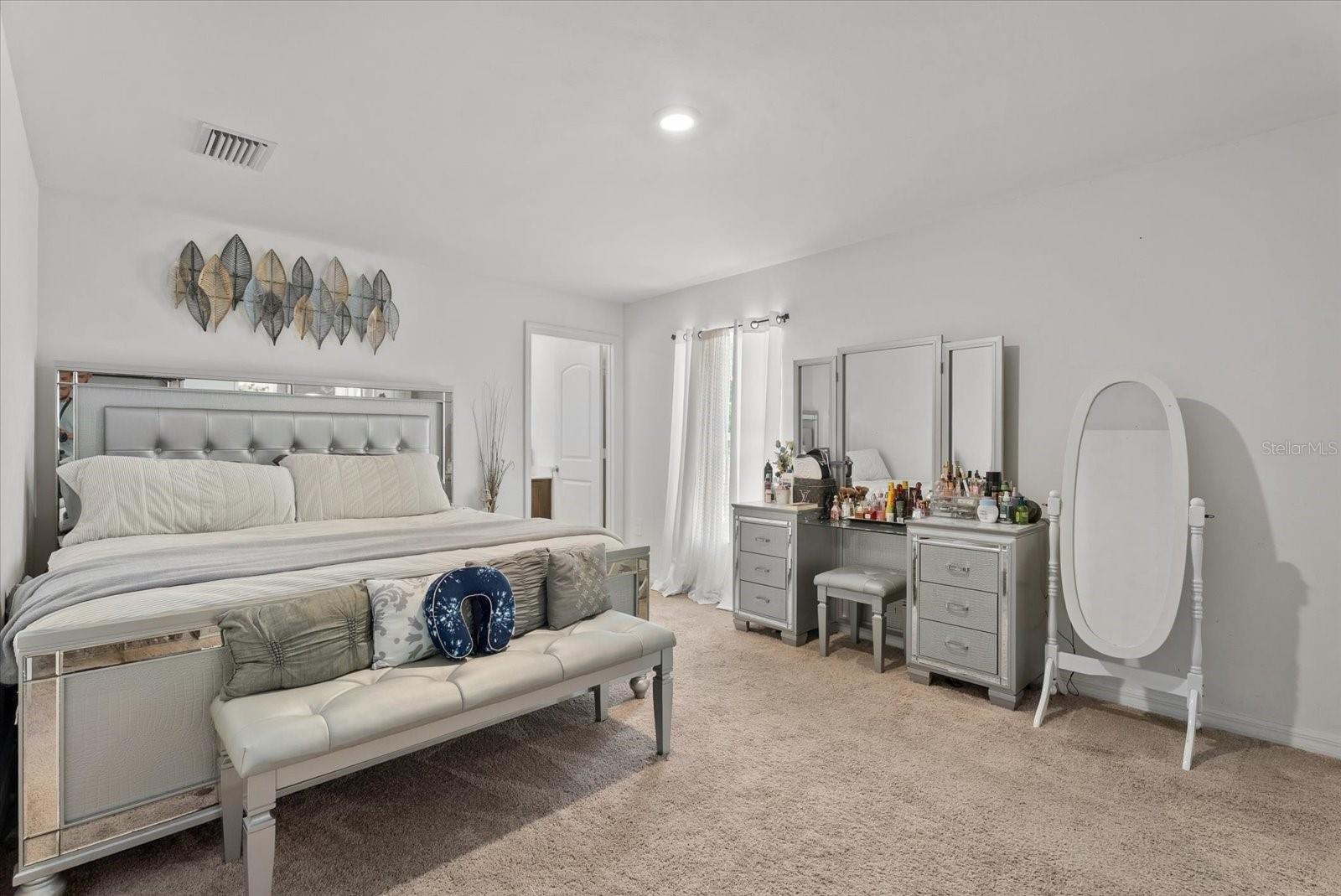 Bedroom with a mirrored tufted headboard, upholstered bench, and vanity.