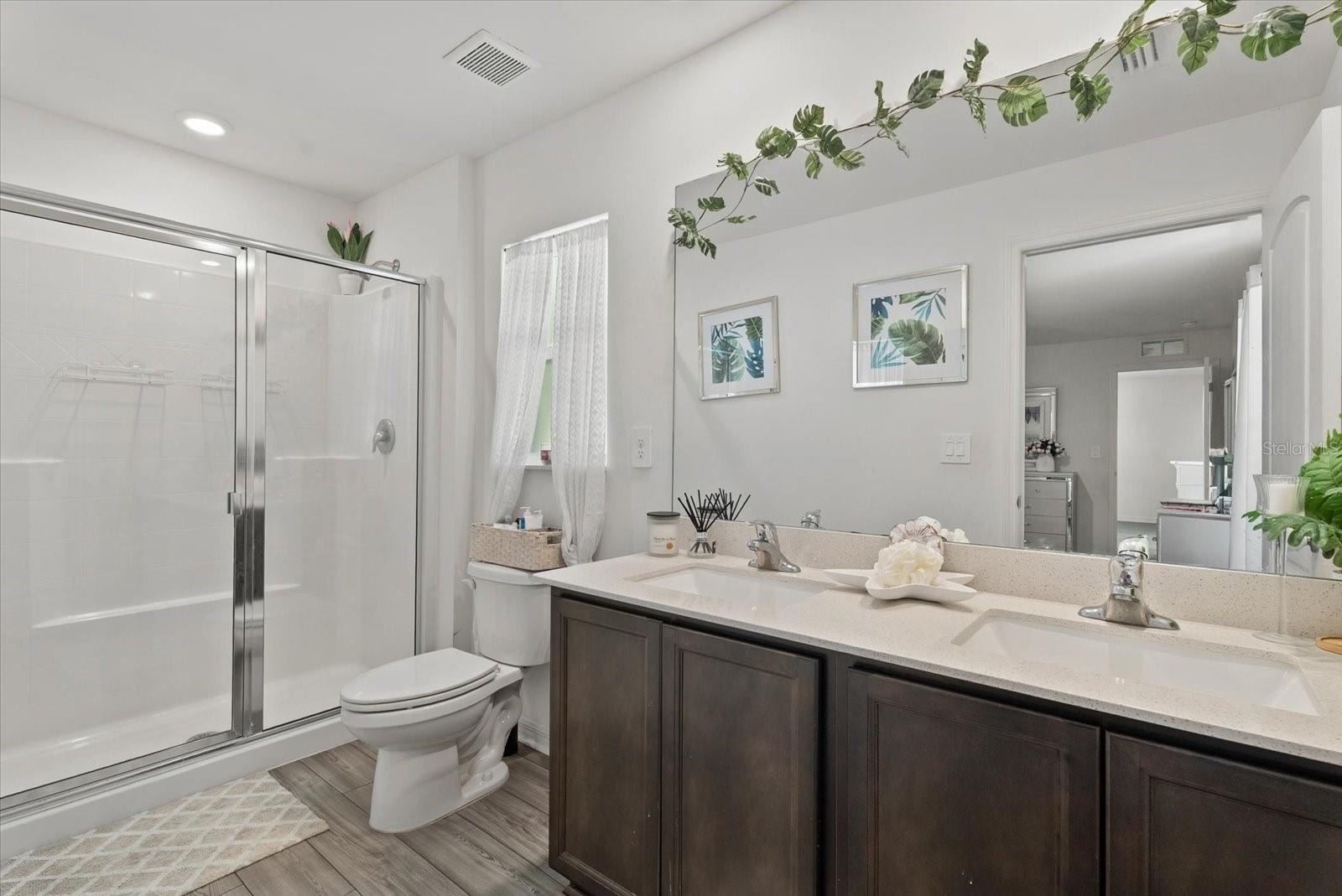 Bathroom with glass shower and double-sink vanity with dark cabinets.