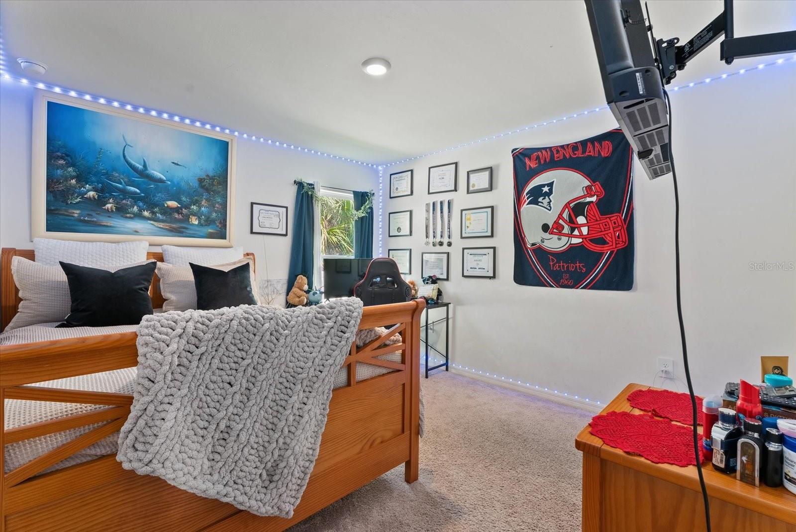Bedroom with a wooden bed, chunky gray blanket, underwater artwork, and a New England Patriots banner.
