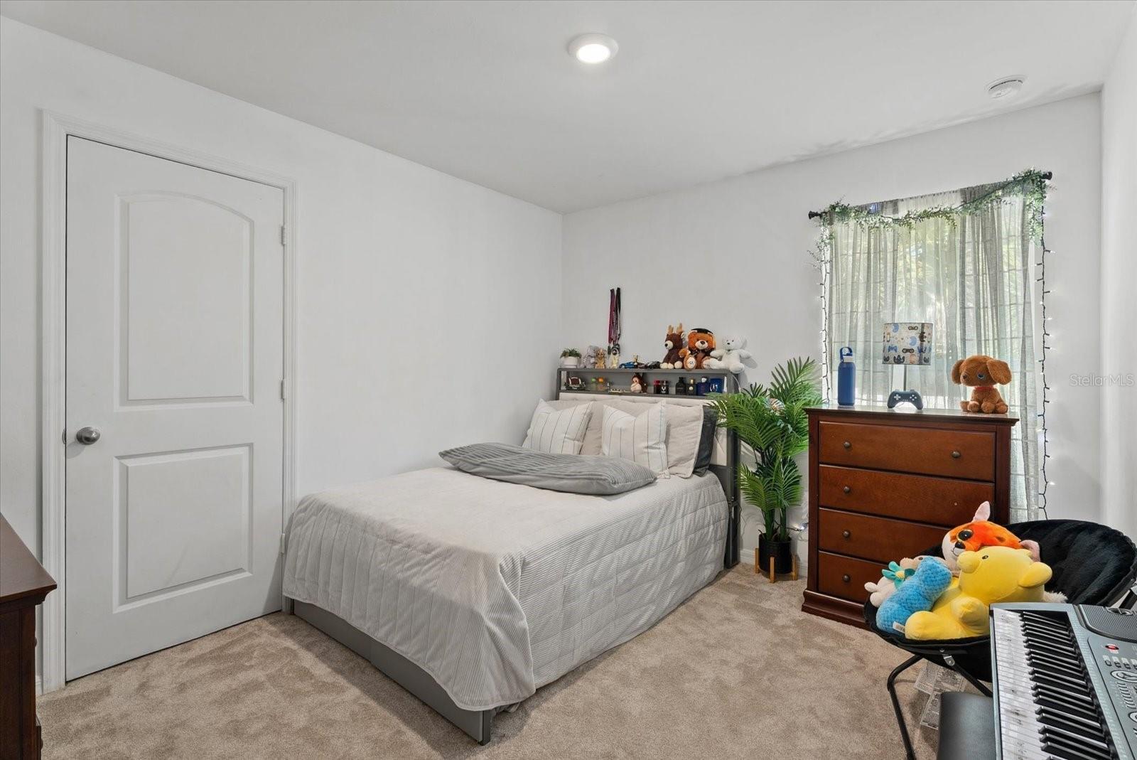 Bedroom with a neatly made bed, dresser, stuffed animals, and a keyboard.