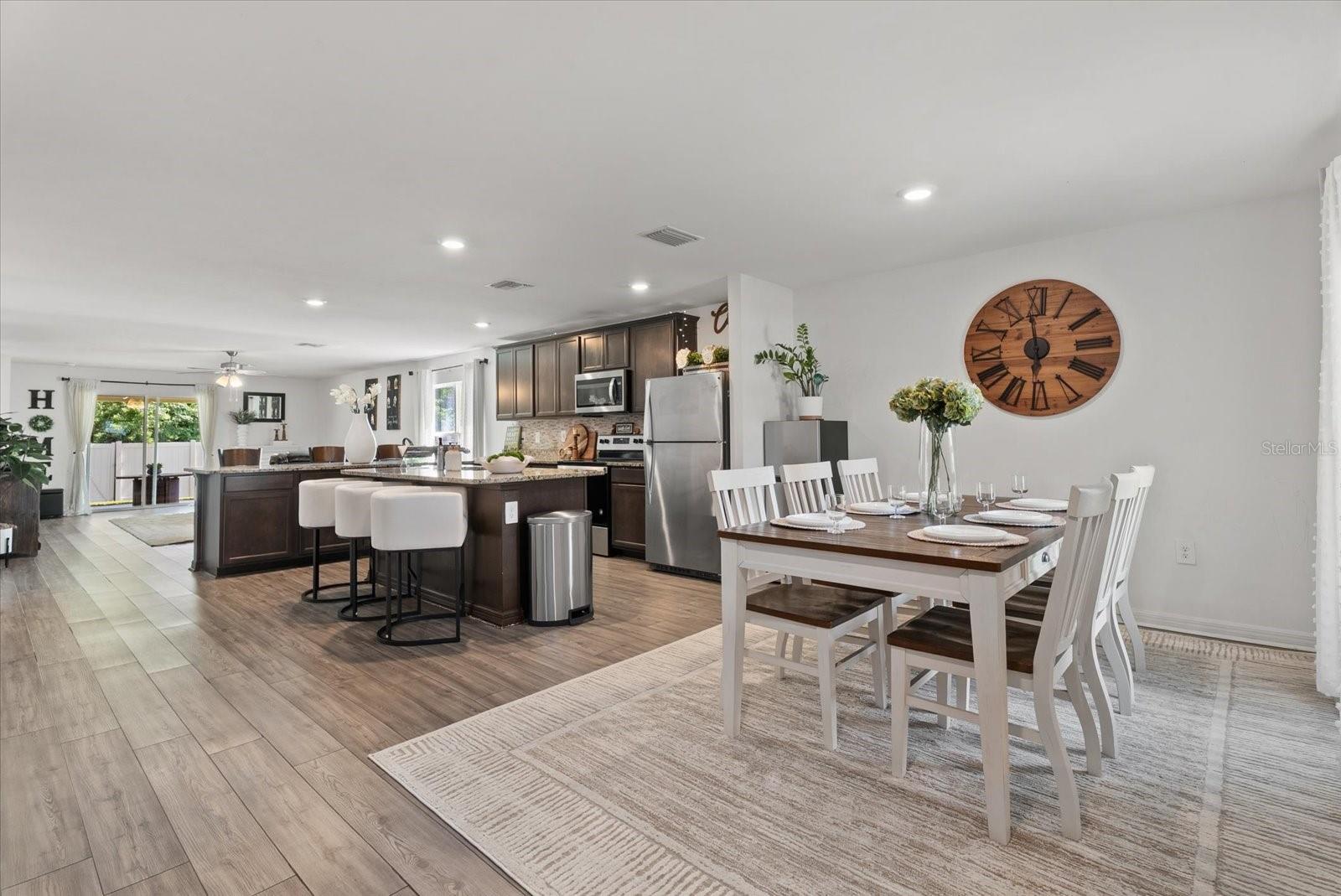 Open-plan kitchen and dining room with a dark island, stainless appliances, and a set dining table.