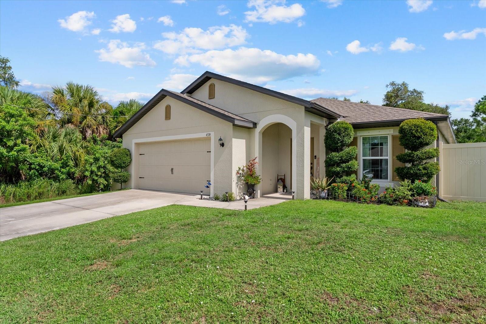 Single-story stucco home with a double garage, arched entry, landscaped garden, and broad front lawn.