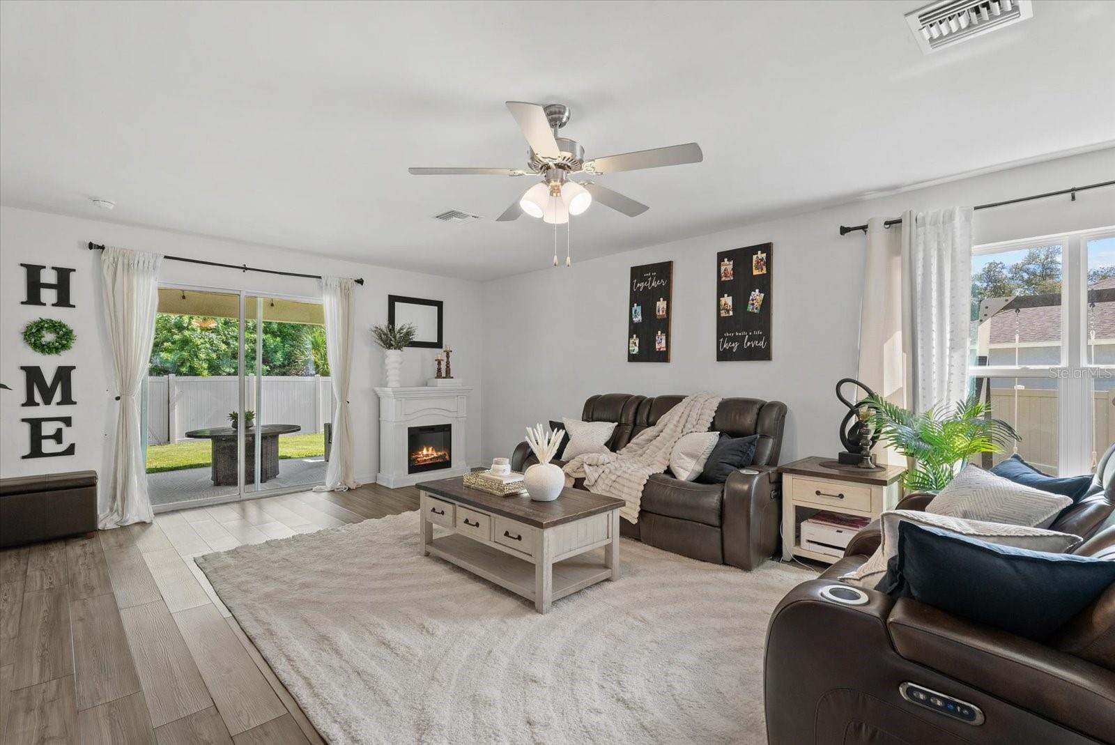 Living room with leather reclining sofas, a white fireplace, and sliding doors to a fenced backyard.