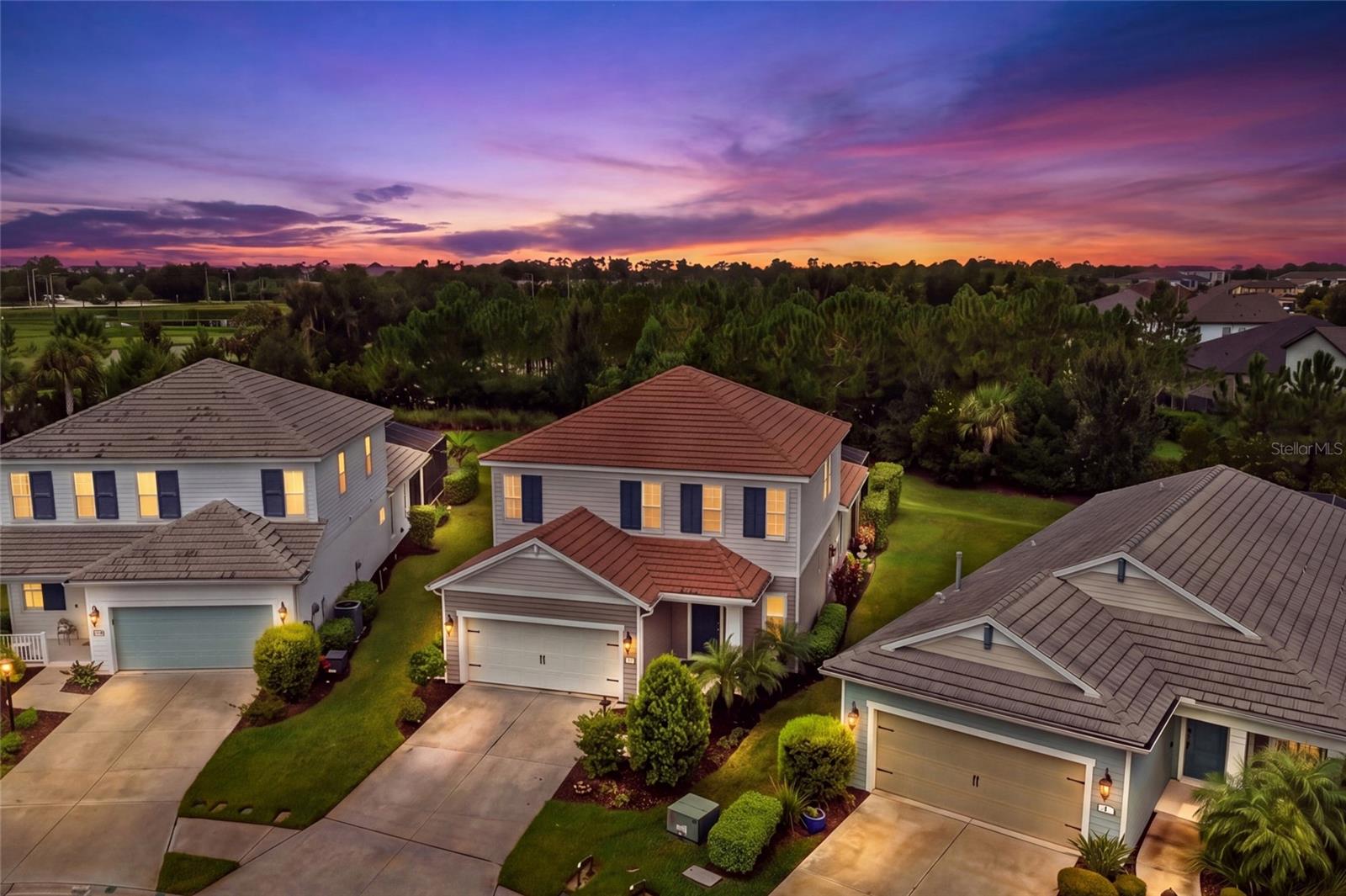 Aerial view of suburban homes and landscaped yards beneath a colorful sunset sky.