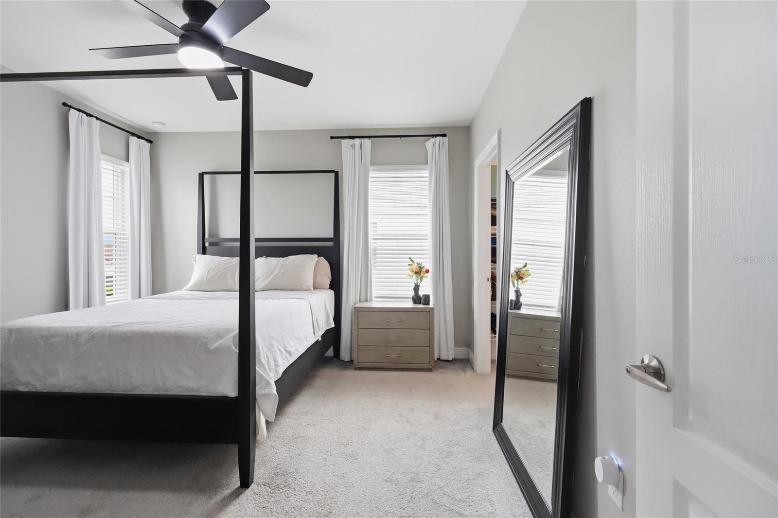 Bedroom with a black four-poster bed, white bedding, and a large leaning mirror.