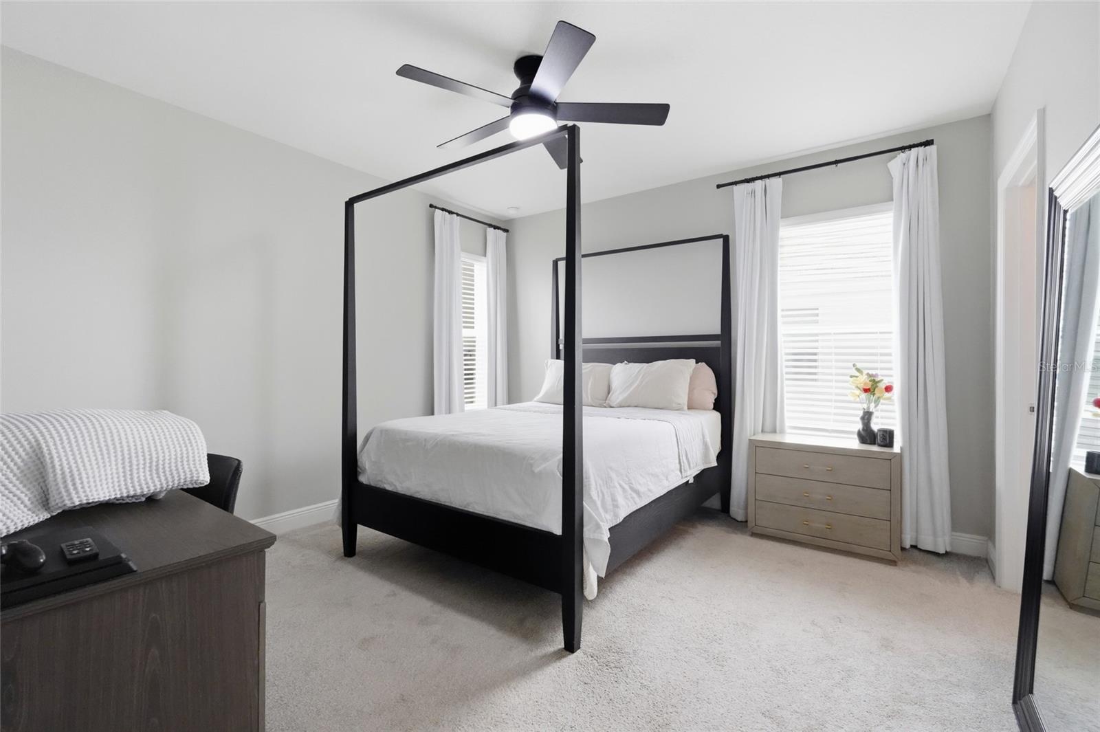 Furnished bedroom with a black four-poster bed, white bedding, and a dresser beside a bright window.