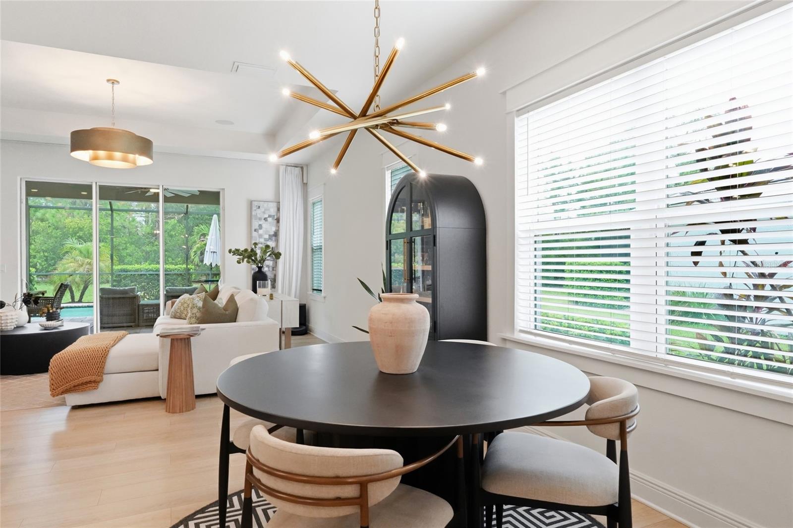 Dining area with a round black table and gold chandelier beside a bright living room.