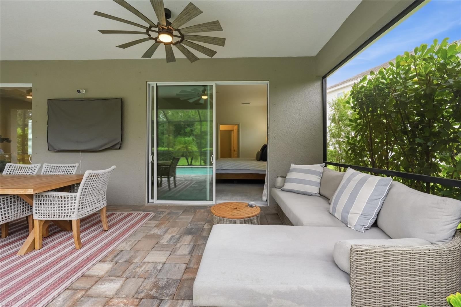 Covered patio with wicker seating and dining area beside a bedroom’s sliding glass door.