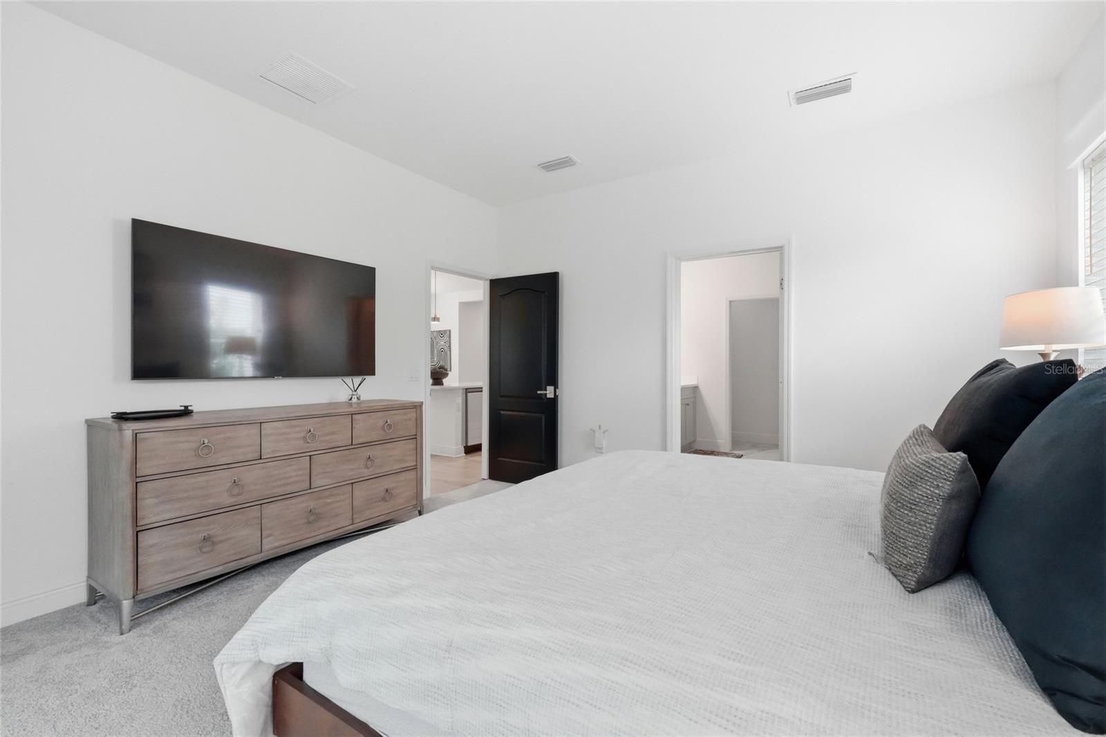 Furnished bedroom with a large bed, dark headboard, and wall-mounted television above a light wood dresser.