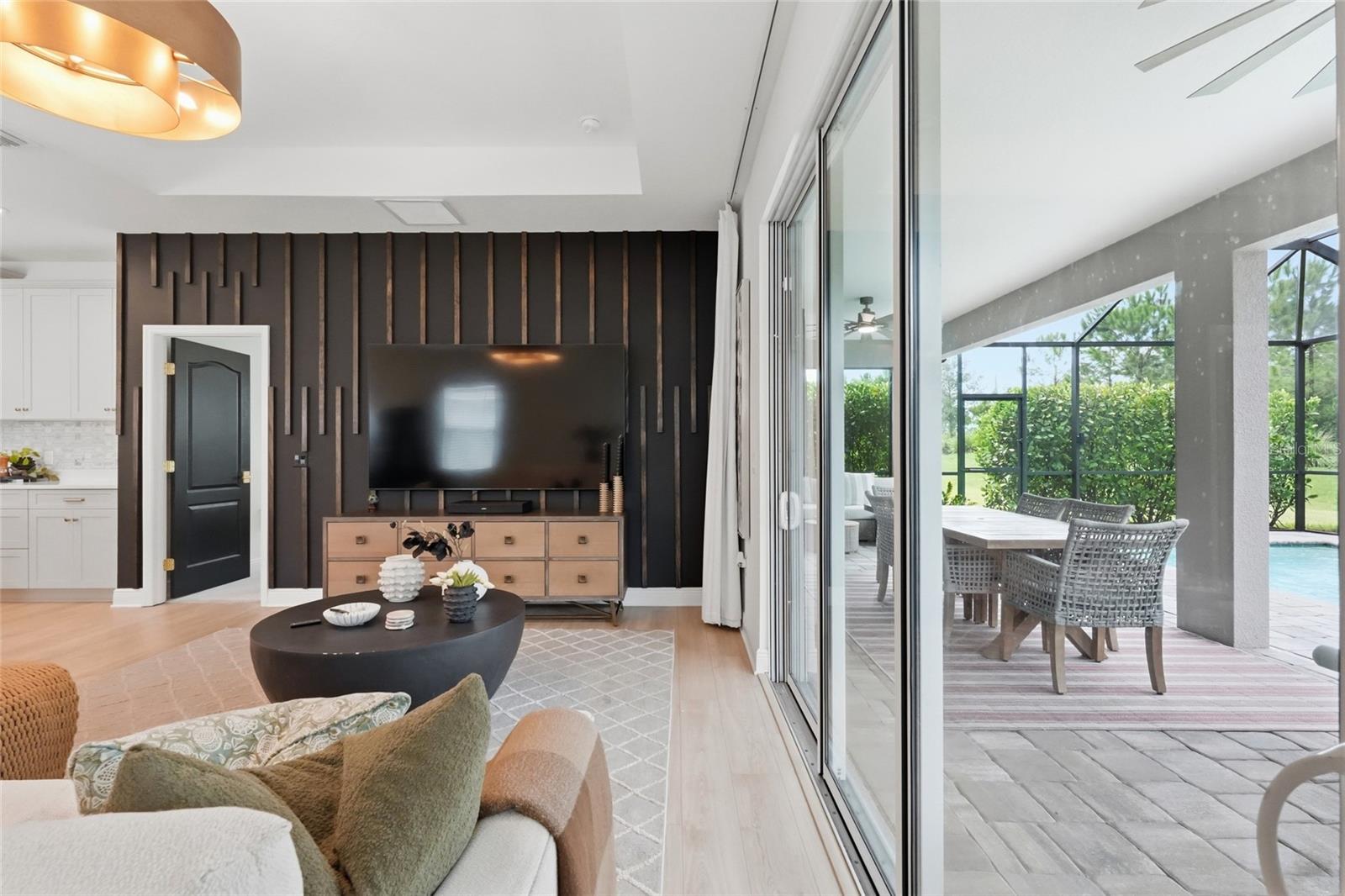 Living room with a dark media wall and sliding doors opening to a covered poolside patio.